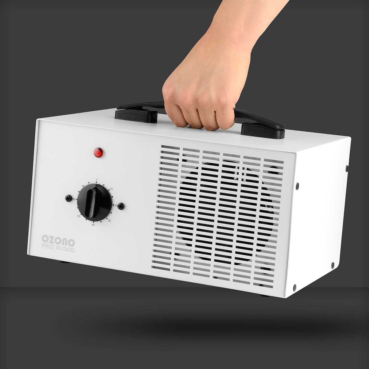 Una máquina de ozono blanca con un asa negra, un dial y rejillas de ventilación. Una mano sostiene el asa.