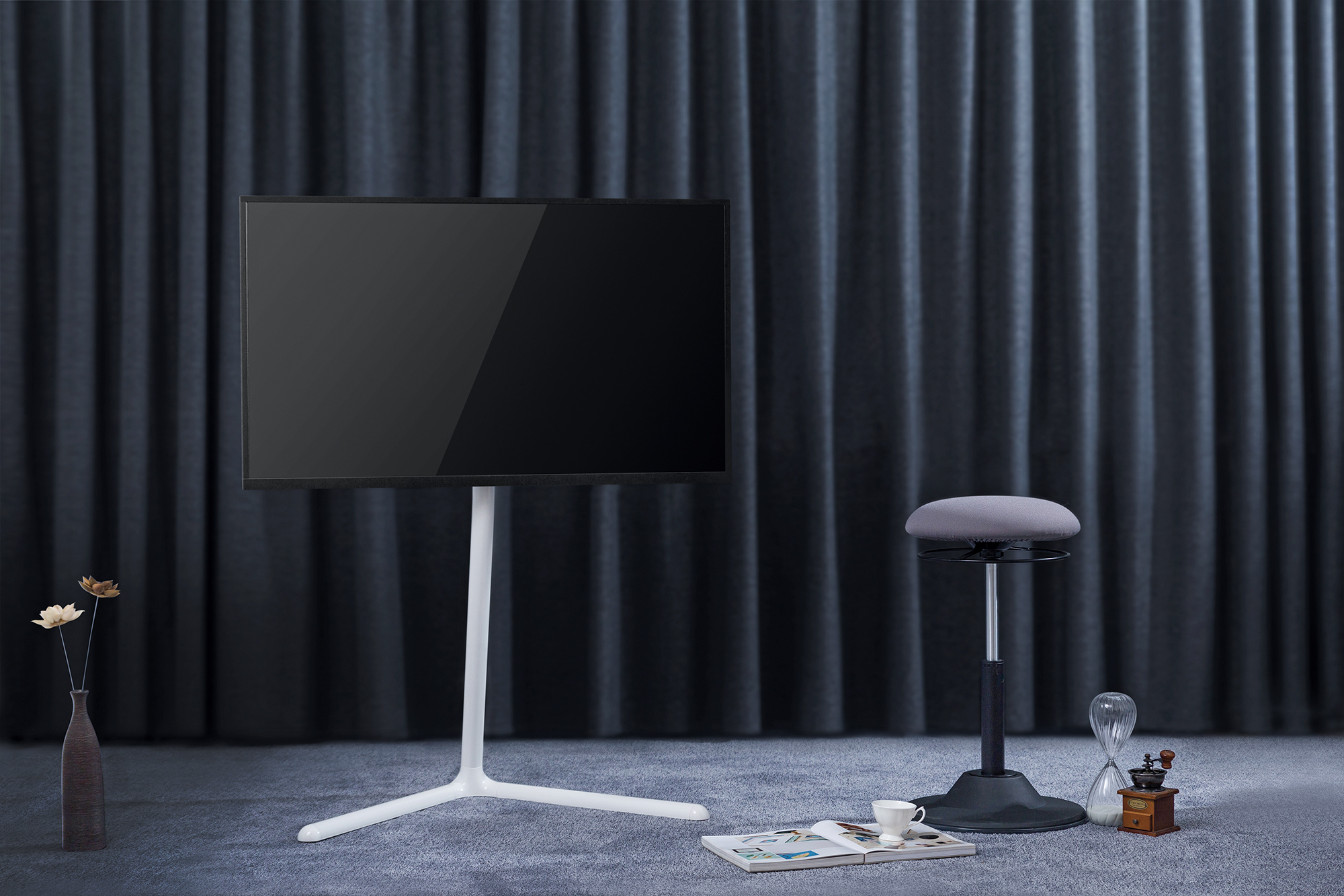Fernseher auf weißem Ständer in einem Raum mit dunklen Vorhängen und Hocker.