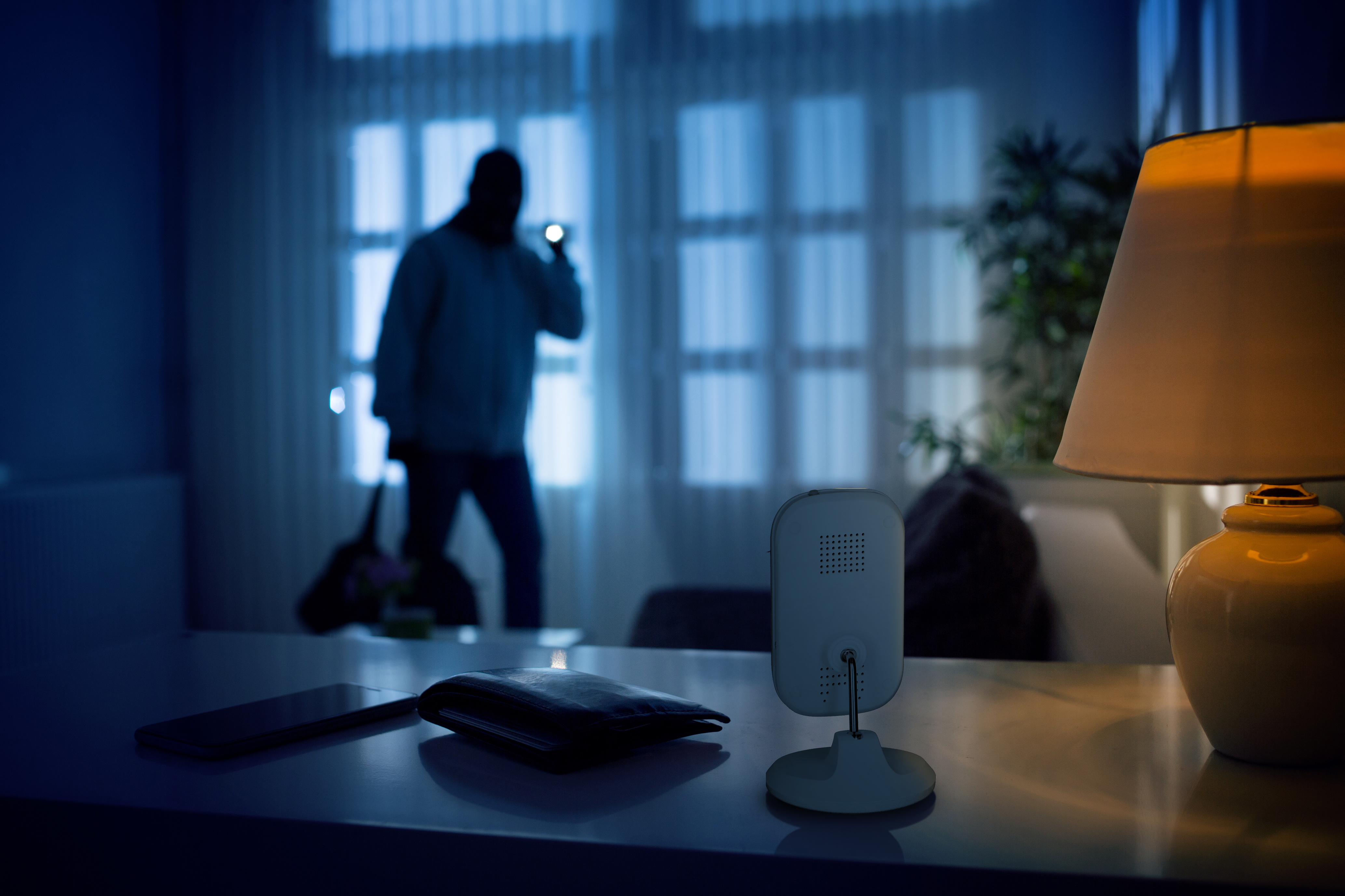 Ein Einbrecher mit Taschenlampe und Tasche in einem dunklen Raum, Überwachungskamera im Vordergrund.