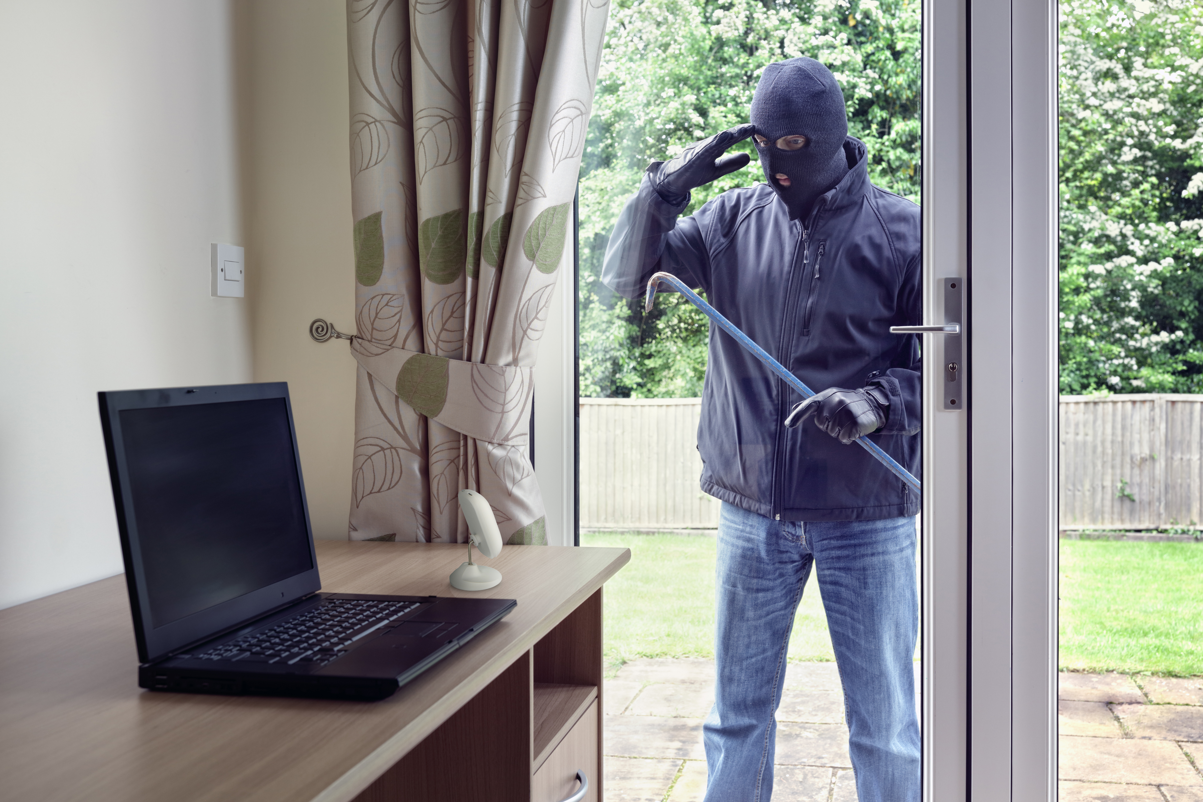 Ein Einbrecher bricht in ein Haus ein. Laptop und Überwachungskamera sind sichtbar.
