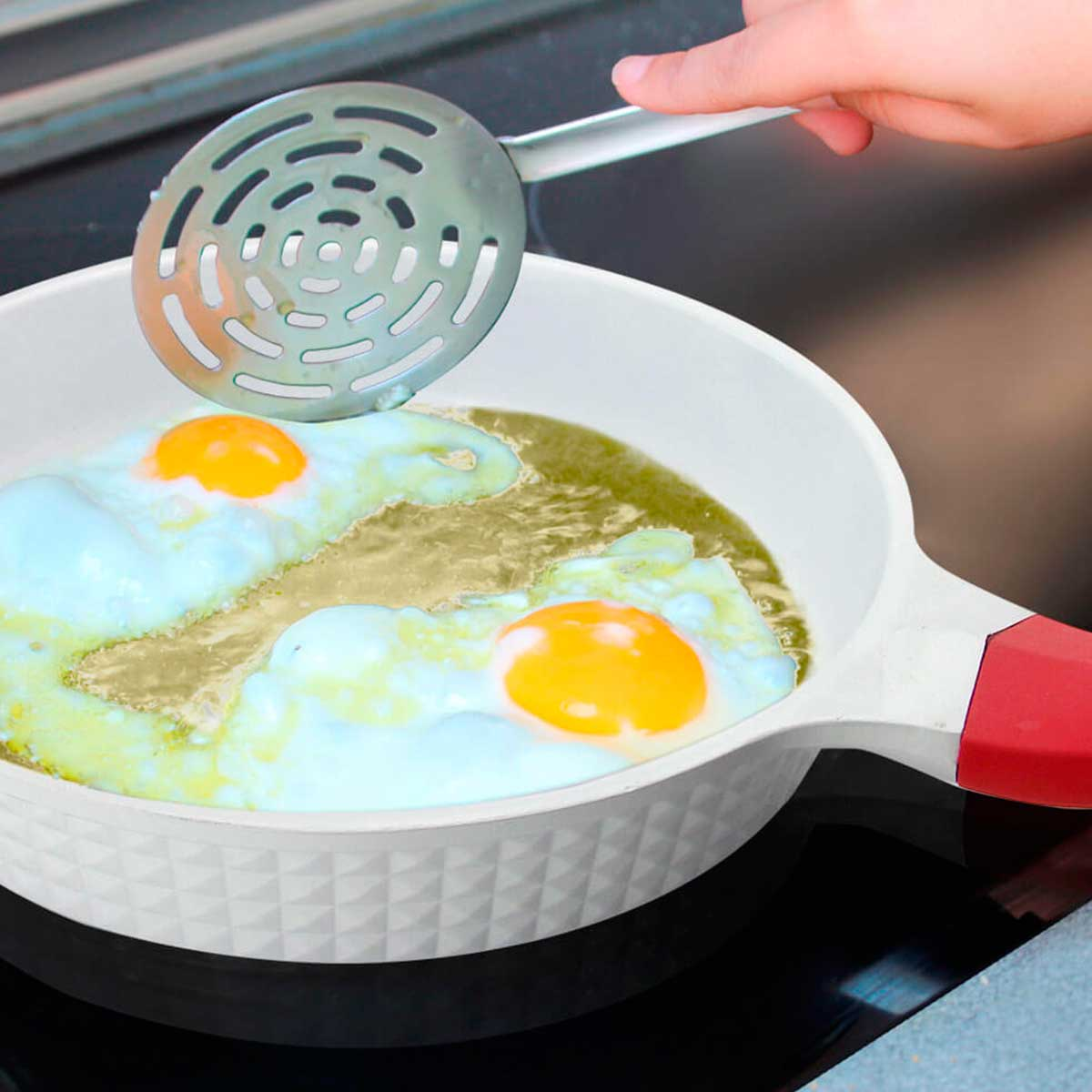 Huevos friéndose en una sartén. Se utiliza una cuchara ranurada para sacarlos.