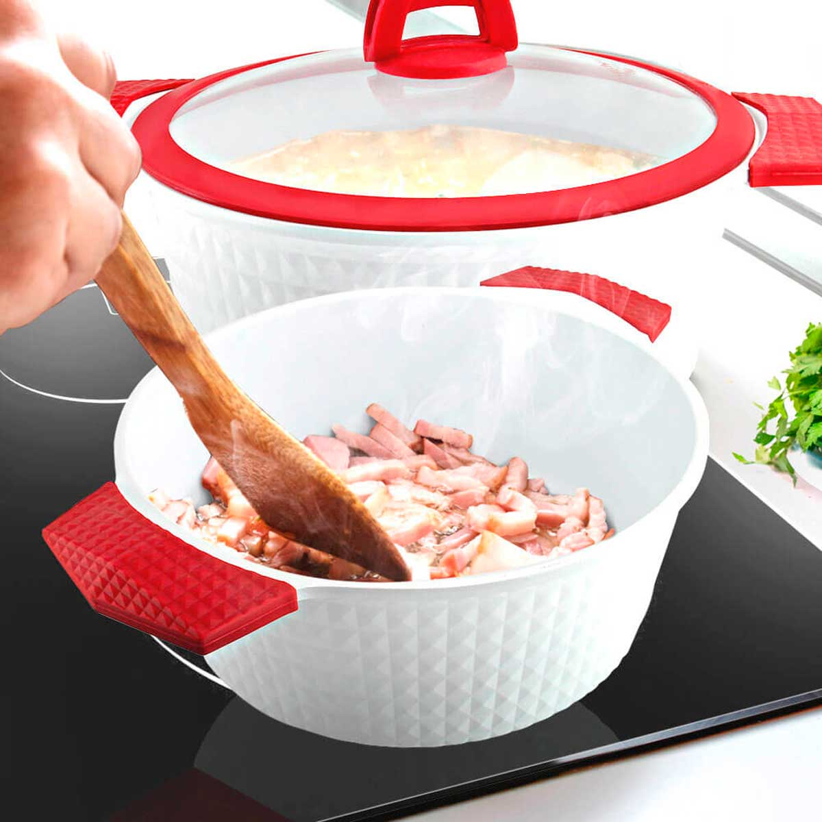 Una olla con comida cocinada que se revuelve con una cuchara de madera. Hay una tapa de vidrio y asas rojas.
