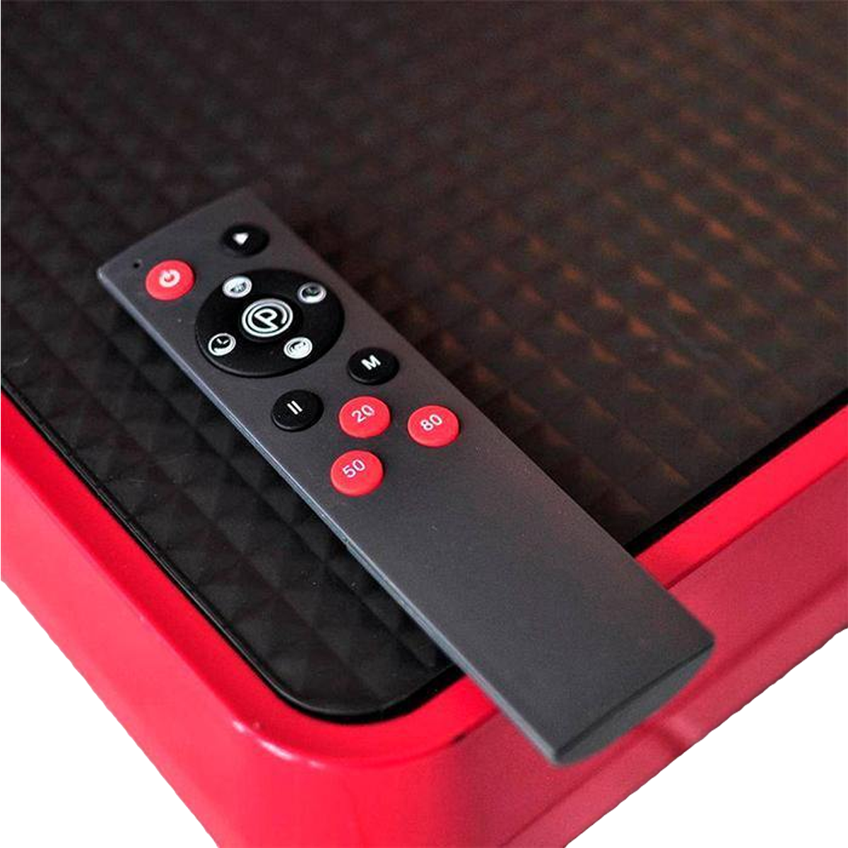 Eine schwarze Fernbedienung mit roten Knöpfen, die auf einer roten und schwarzen Vibrationsplatte liegt.