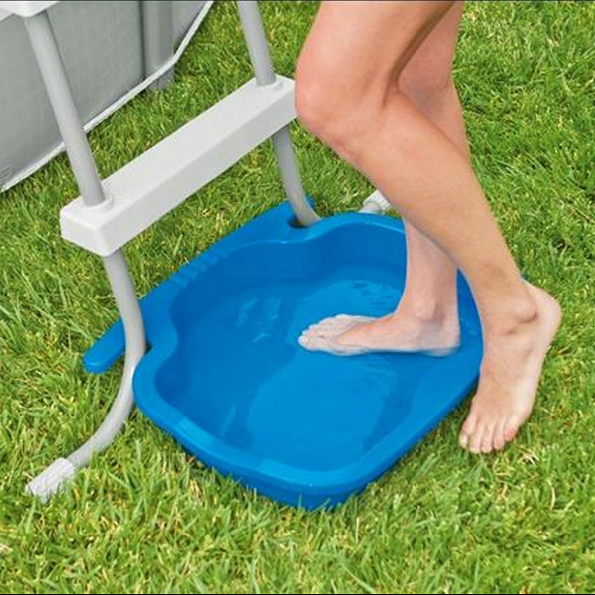 Voeten van een persoon in een blauw voetbad, naast een zwembadladder, op een grasveld.