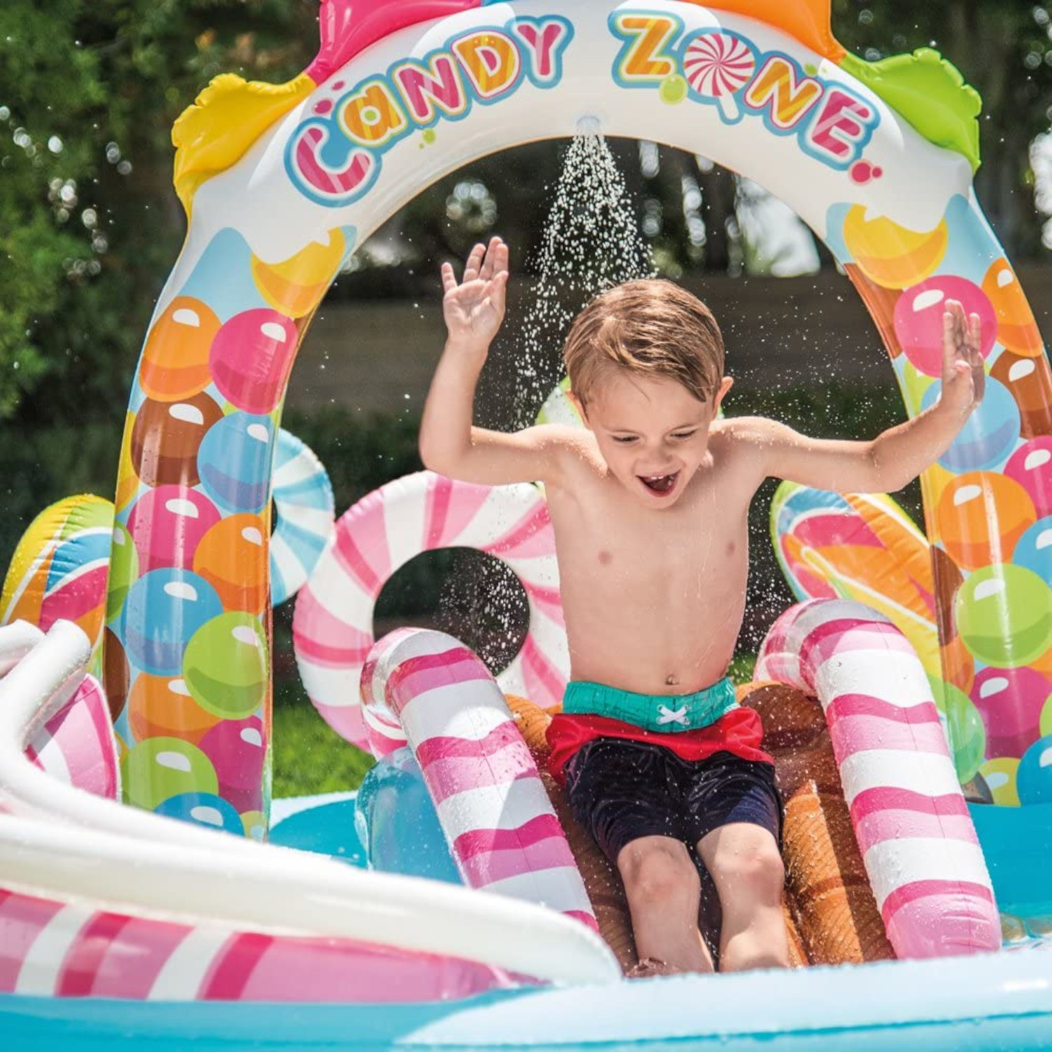 Un bambino gioca in un parco acquatico gonfiabile a tema caramelle con uno scivolo.
