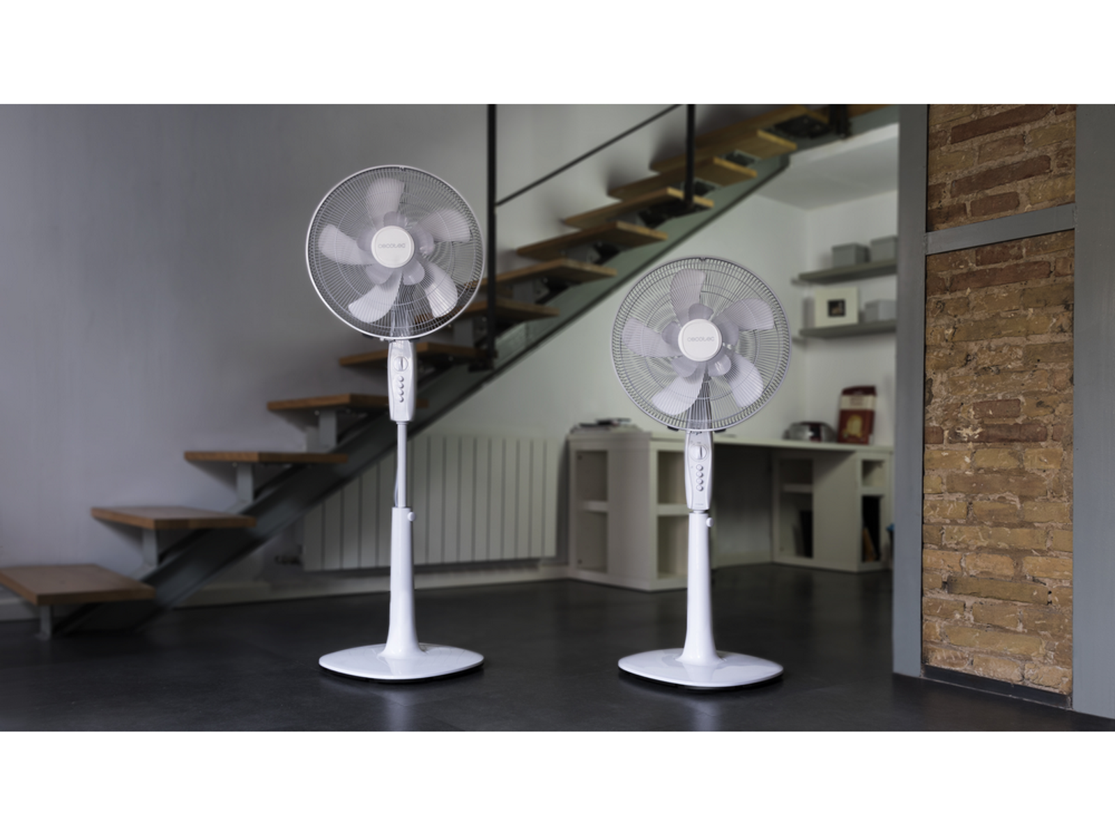 Dwa białe wentylatory stojące z wieloma łopatkami, w pomieszczeniu ze schodami i biurkiem.