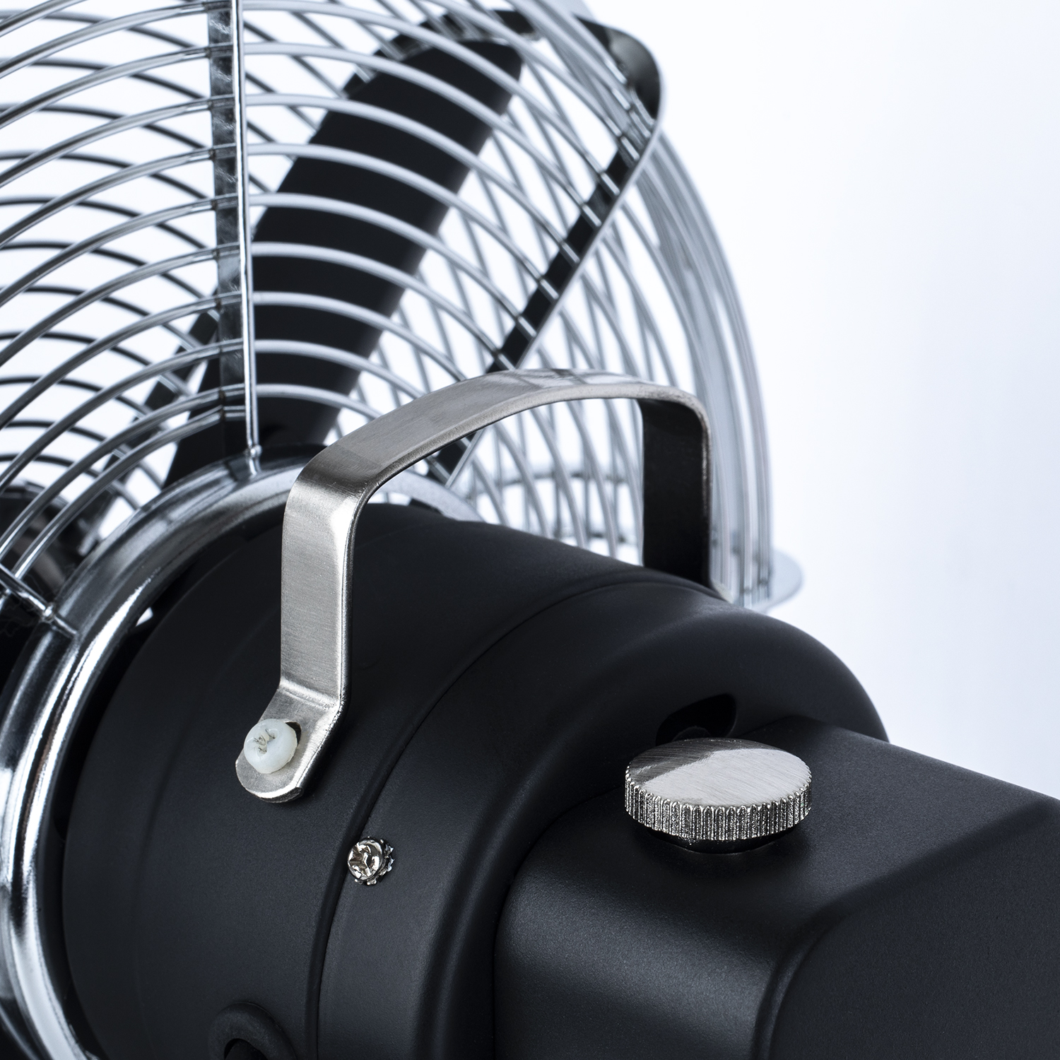 Primo piano di un ventilatore nero con griglia e maniglia cromate. Una manopola è visibile.