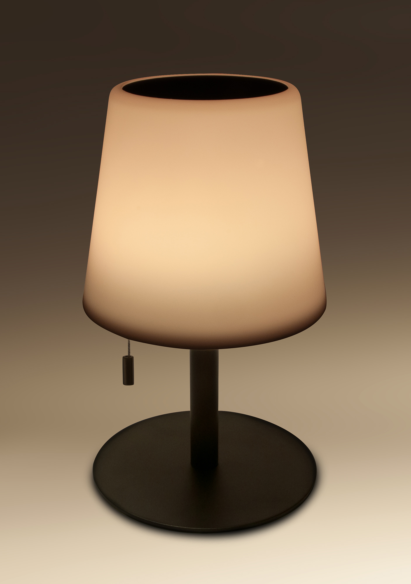Eine weiße Lampe mit schwarzem Sockel. Die Lampe ist eingeschaltet. Licht kommt von oben.