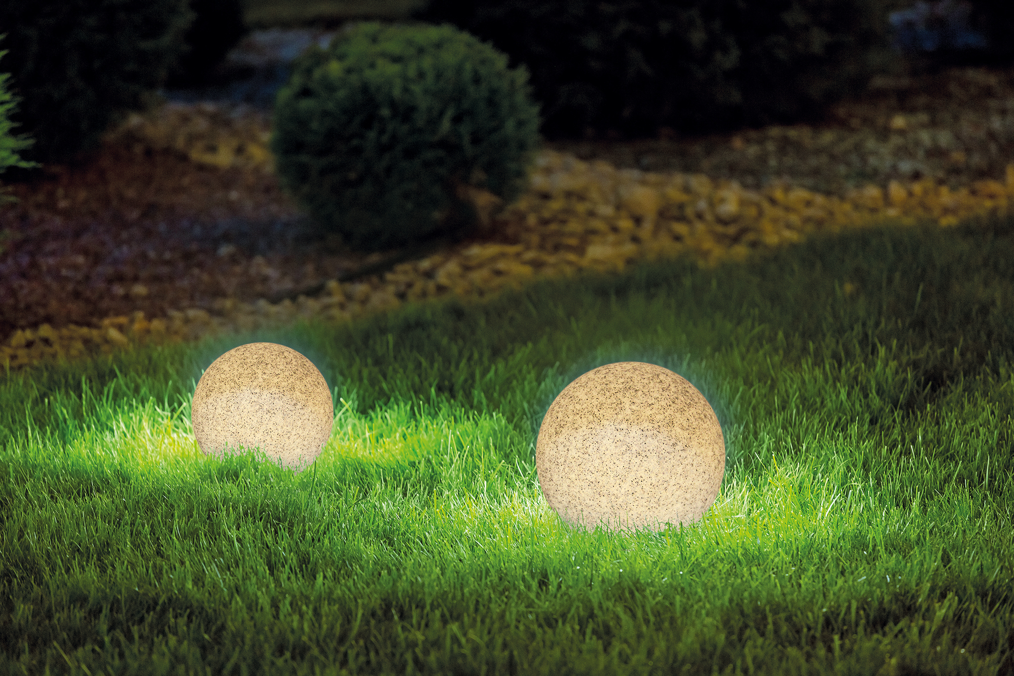 Zwei beleuchtete, steinartige Außenleuchten auf grünem Gras unter Nachthimmel.