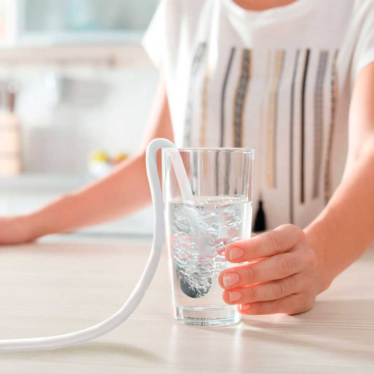 Mano sosteniendo vaso con agua, tubo blanco y objeto dentro.