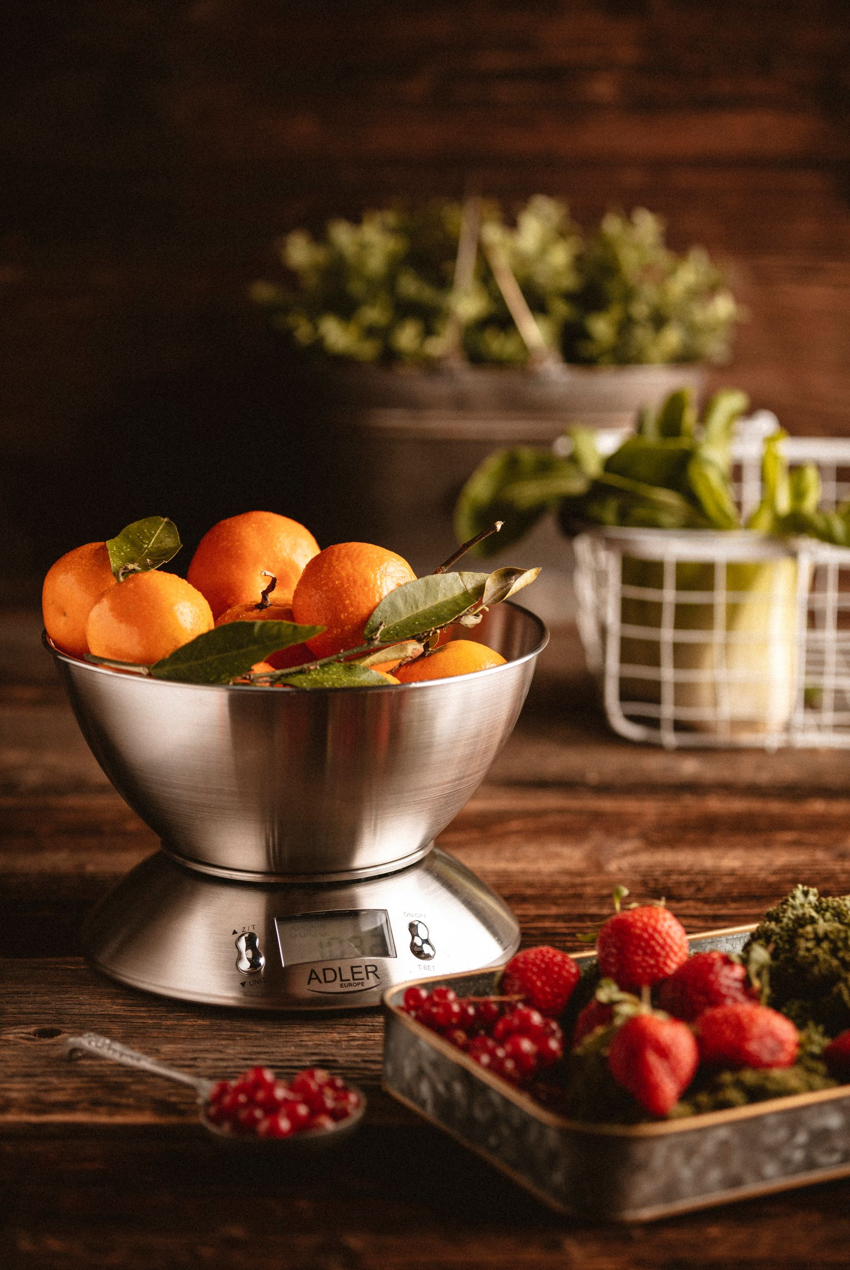 Miska pomarańczy na wadze, z innymi składnikami. Zawiera truskawki, zieleń i łyżkę nasion.