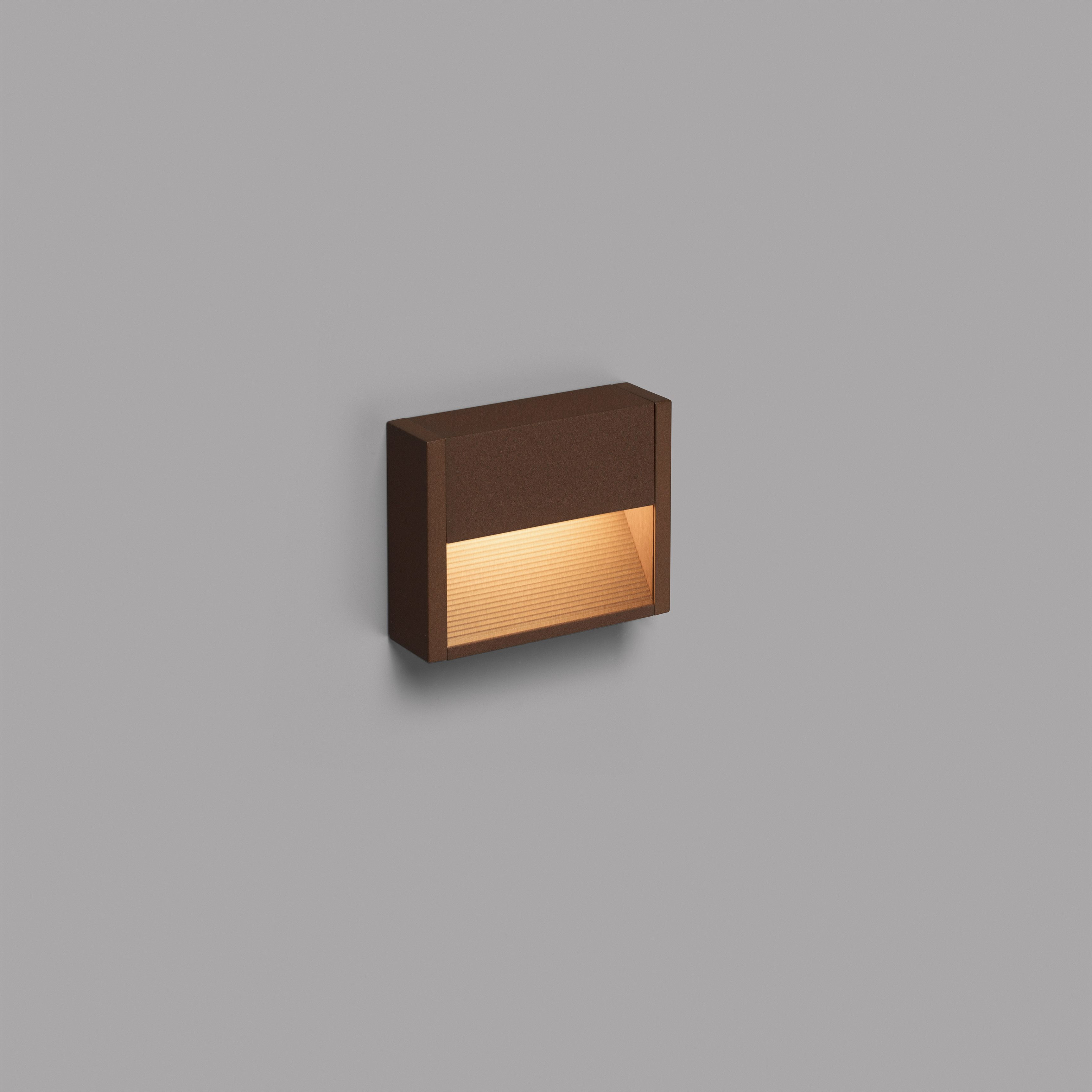 Una lampada da parete quadrata marrone con luce che brilla dal basso.