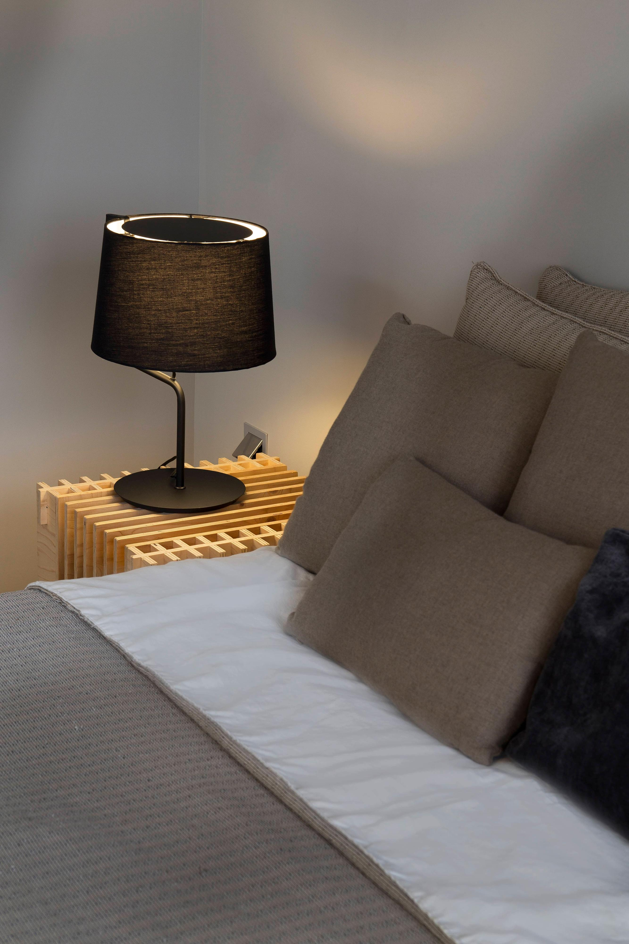 Una scena della camera da letto con una lampada su un comodino e cuscini sul letto.