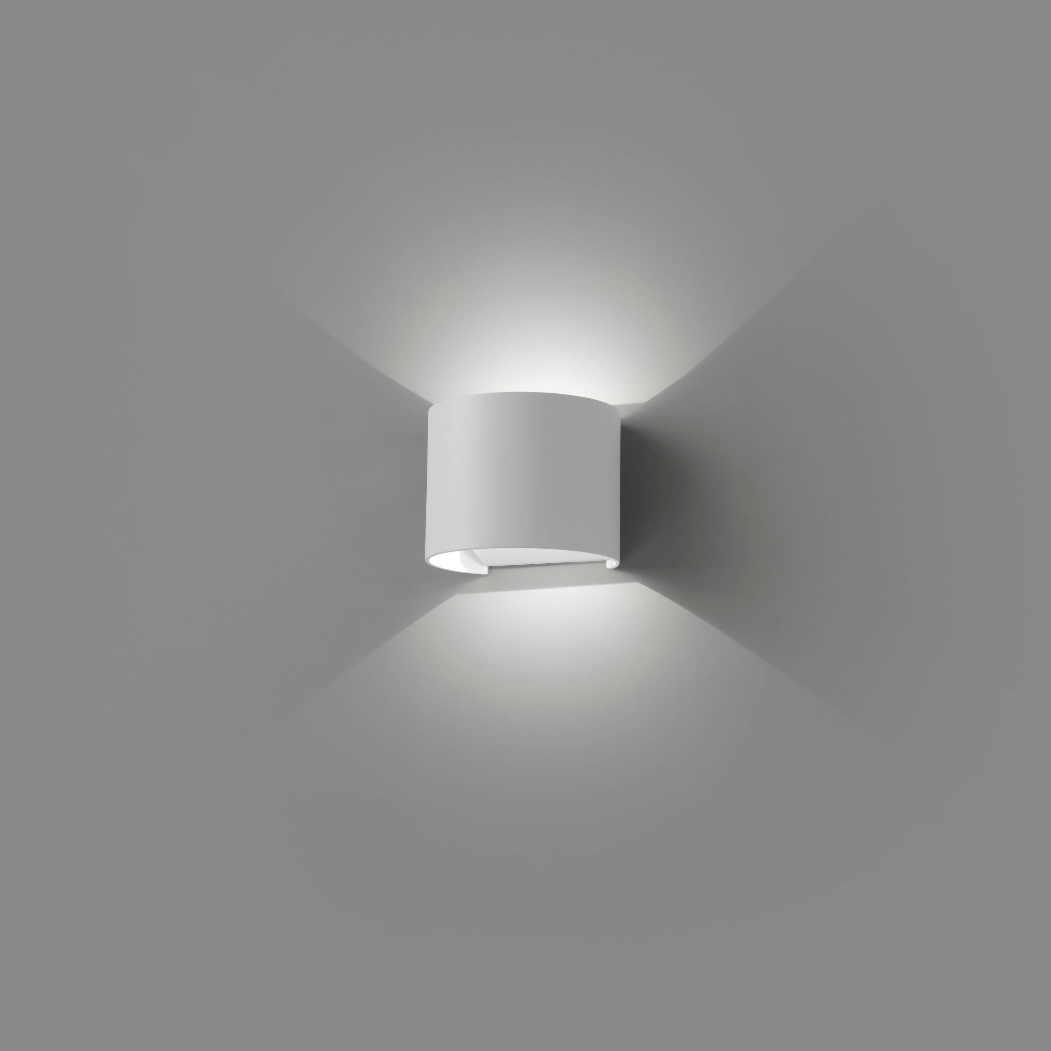 Un'applique da parete bianca, che emette luce. Ha un design curvo e proietta ombre.