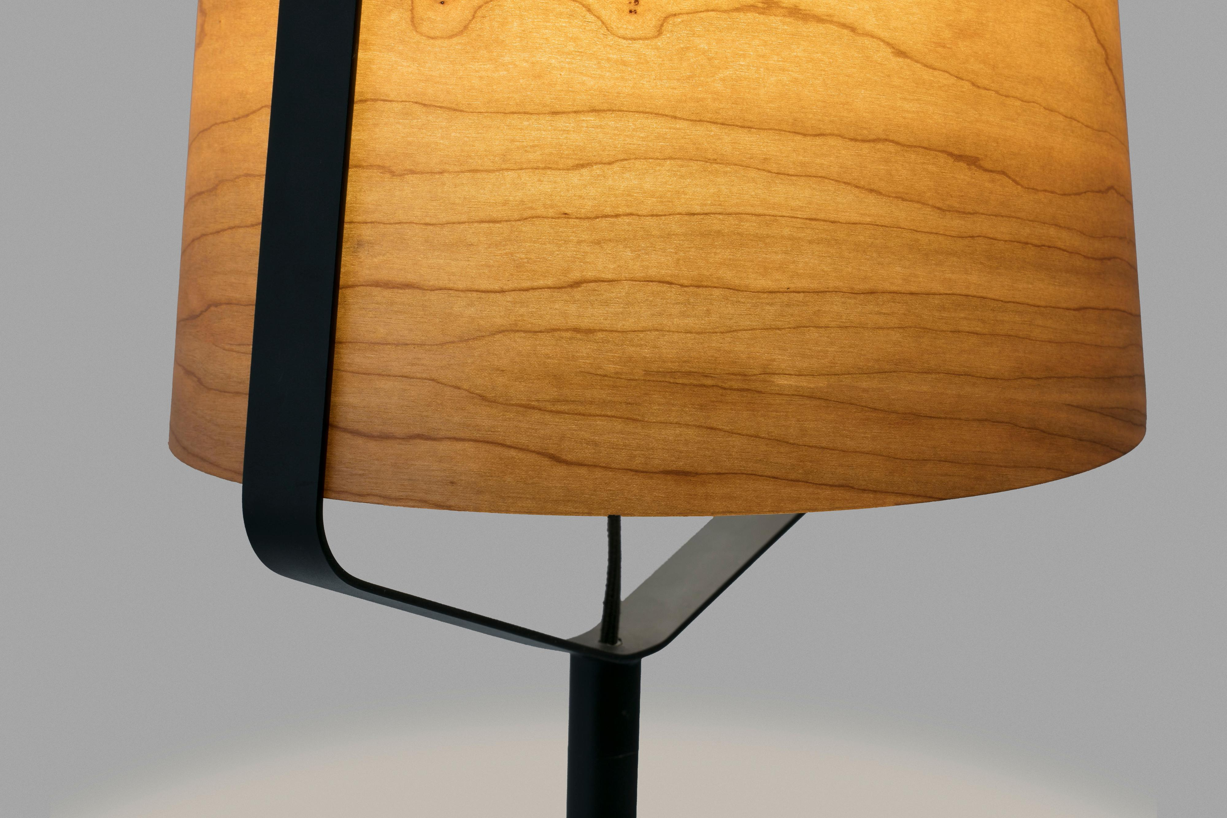 Una lampada con paralume in legno e telaio nero. La luce proviene dall'interno.