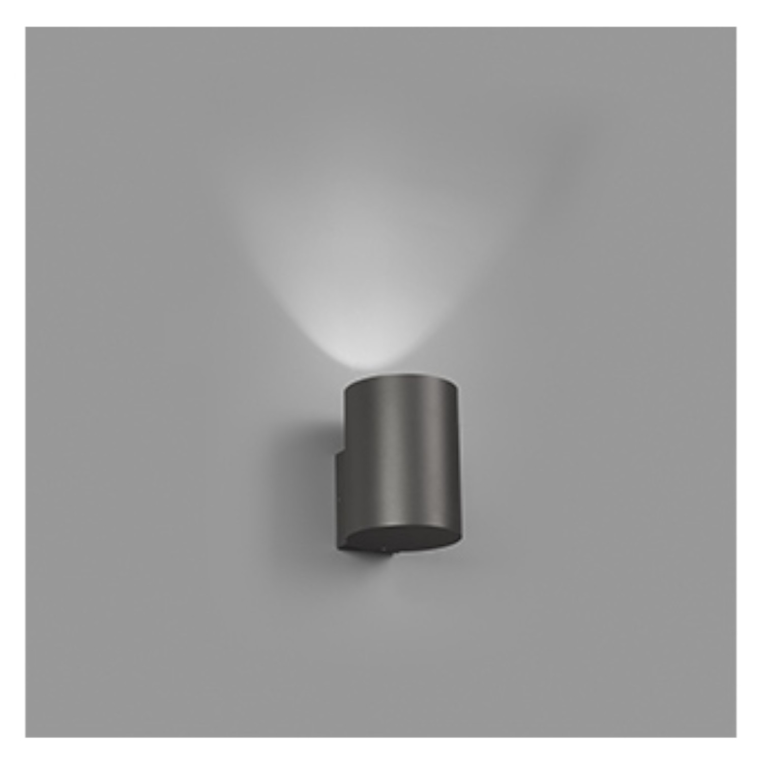 Una lampada da parete cilindrica con un fascio di luce su un muro grigio.
