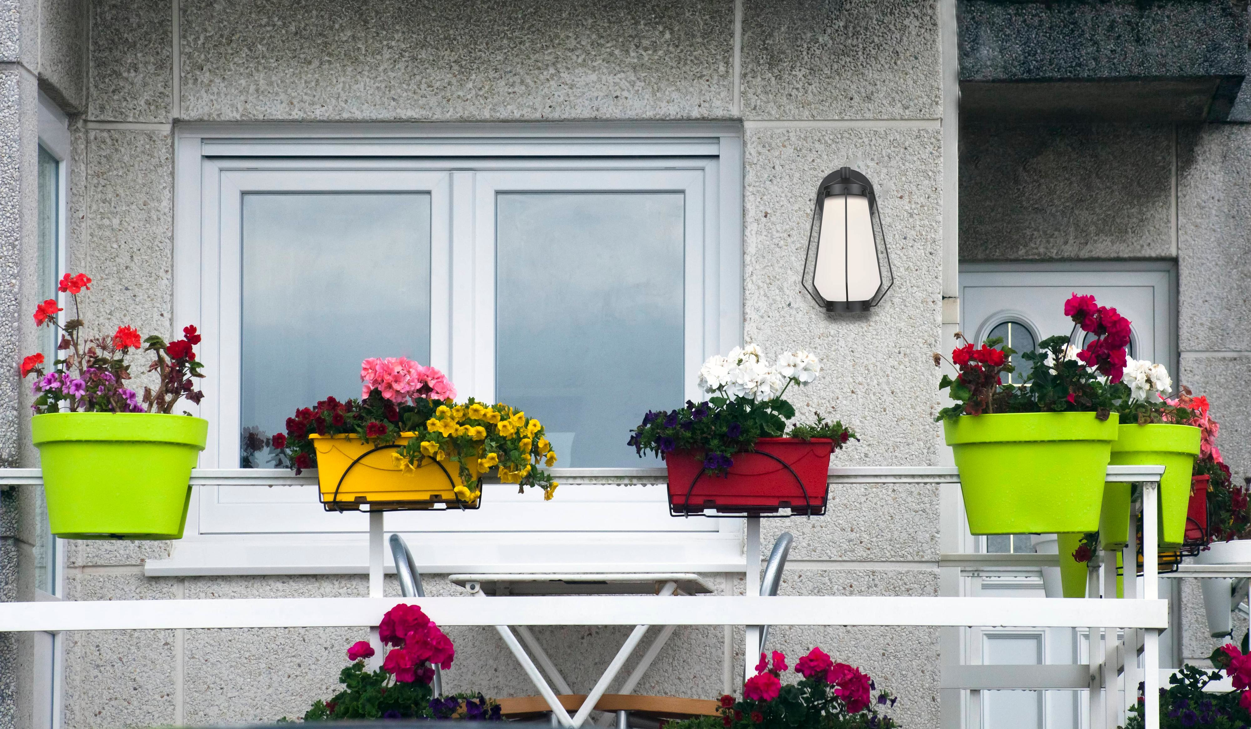Ein Balkon mit bunten Blumenkästen, weißem Geländer und Wandleuchte.