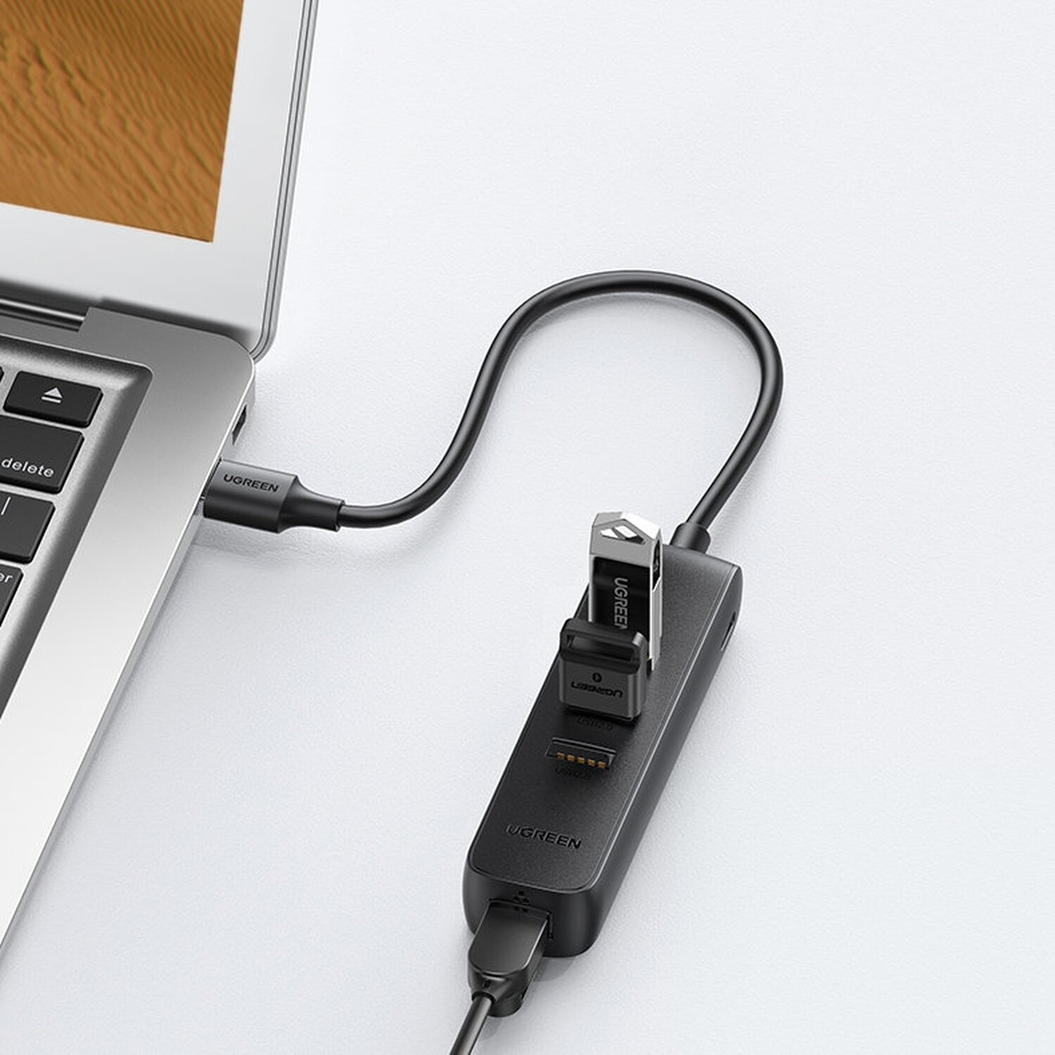 Ein UGREEN-Hub, der mit einem Laptop verbunden ist, mit einem USB-Laufwerk und anderen Anschlüssen. Das Setup befindet sich auf einer weißen Oberfläche.