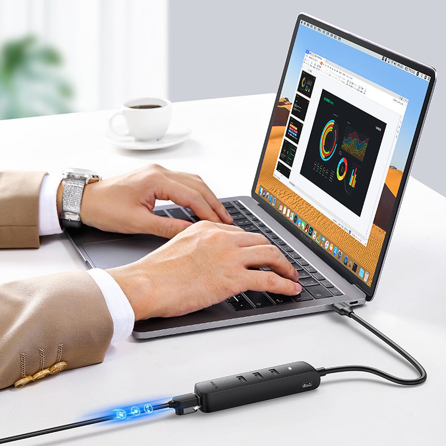 Ein Mann benutzt einen Laptop, der mit einem schwarzen USB-Hub mit Lichtern verbunden ist, auf einem weißen Schreibtisch, mit Kaffeetasse.