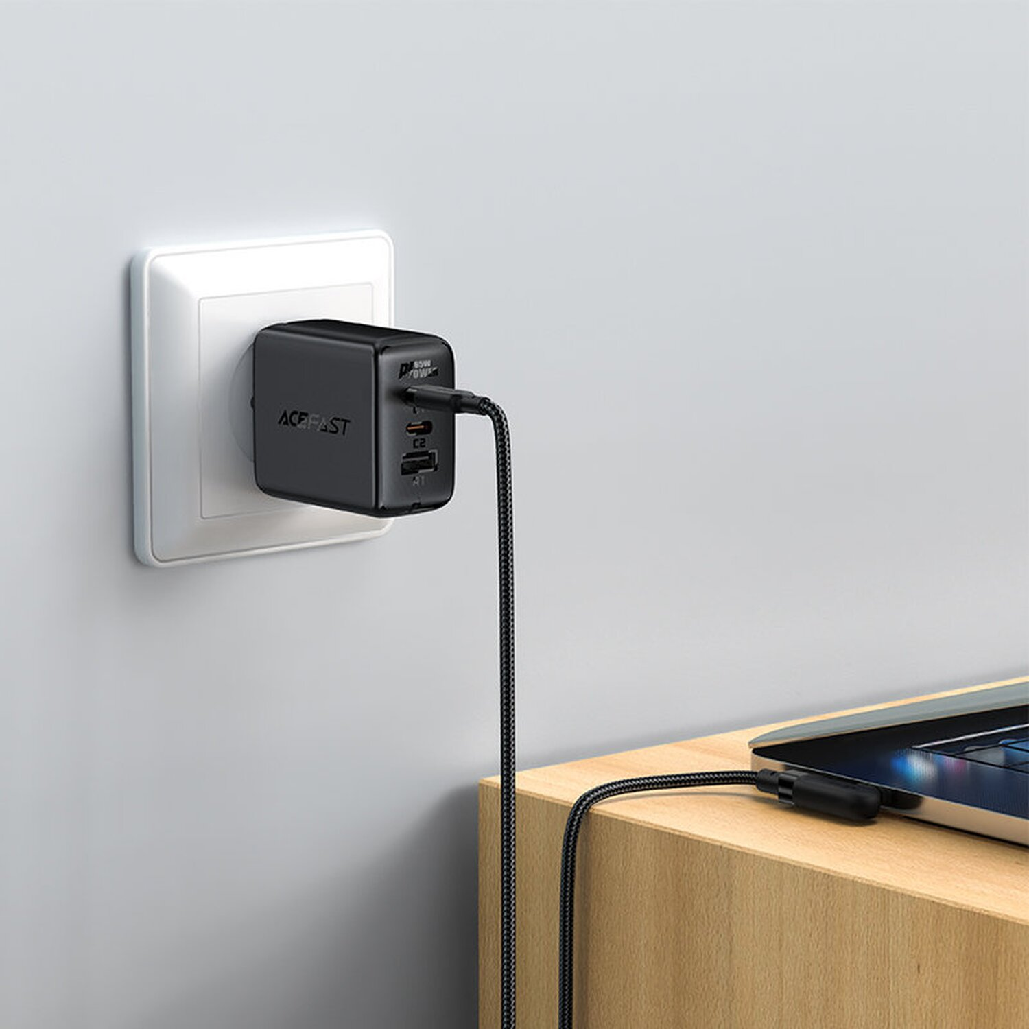 Schwarzes USB-Ladegerät, das in eine Steckdose gesteckt ist und einen Laptop über ein USB-C-Kabel lädt.