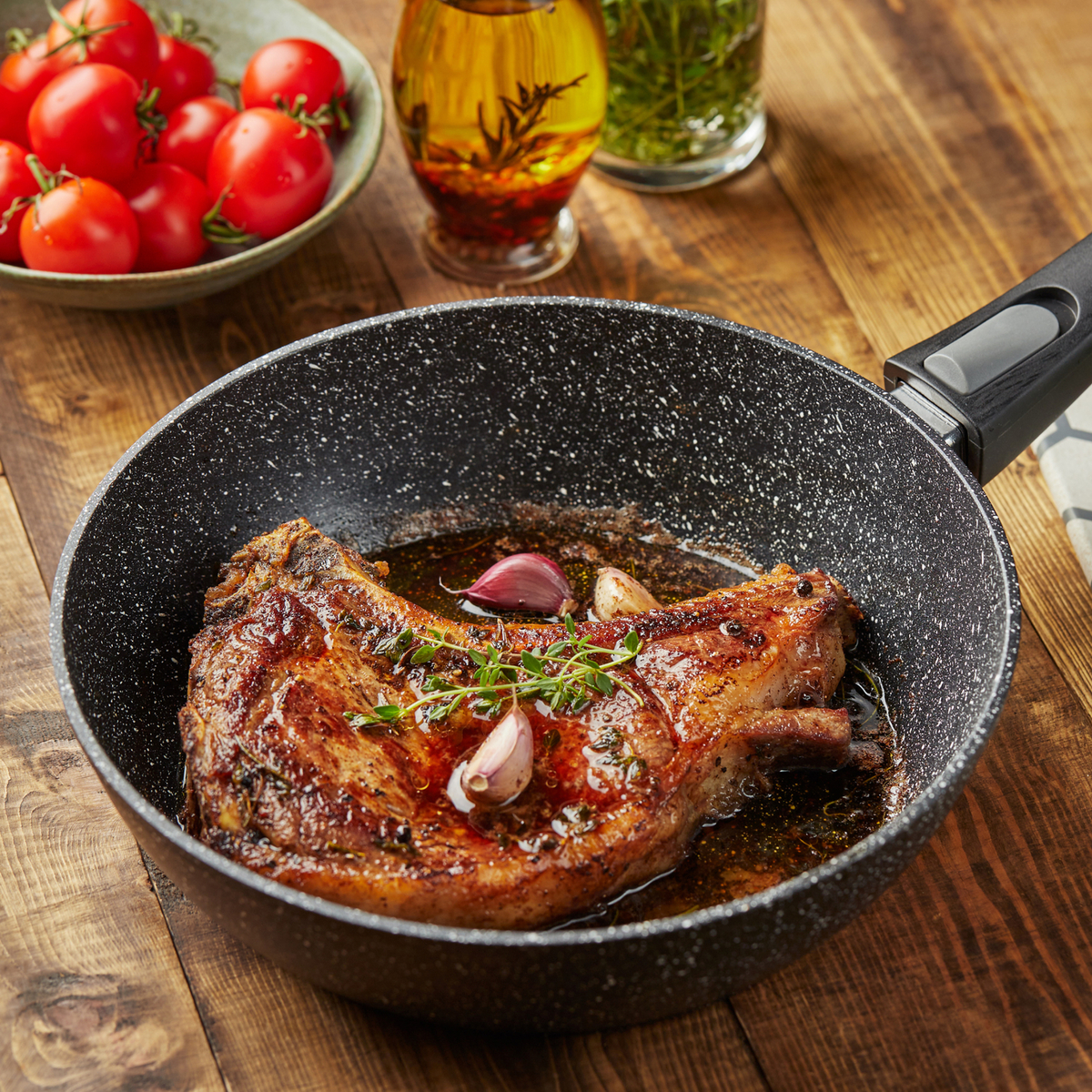 Une côte de porc cuite dans une poêle avec de l'ail et des herbes, sur une table en bois.