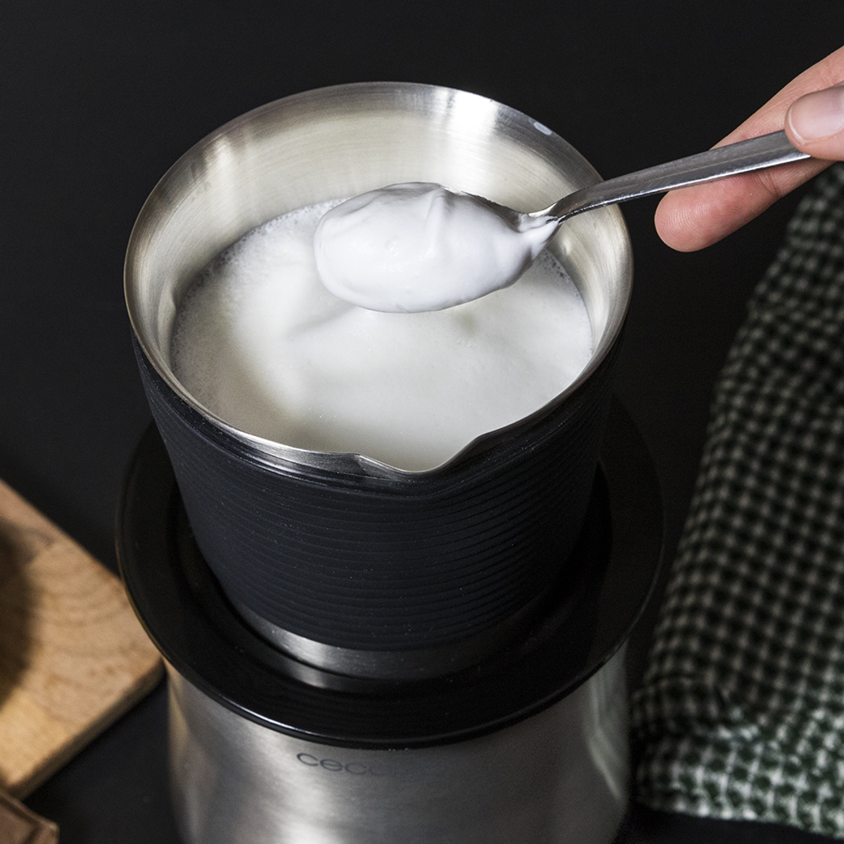 Osoba nabierająca pianę ze srebrnego dzbanka do spieniania mleka do czarnej podstawy.
