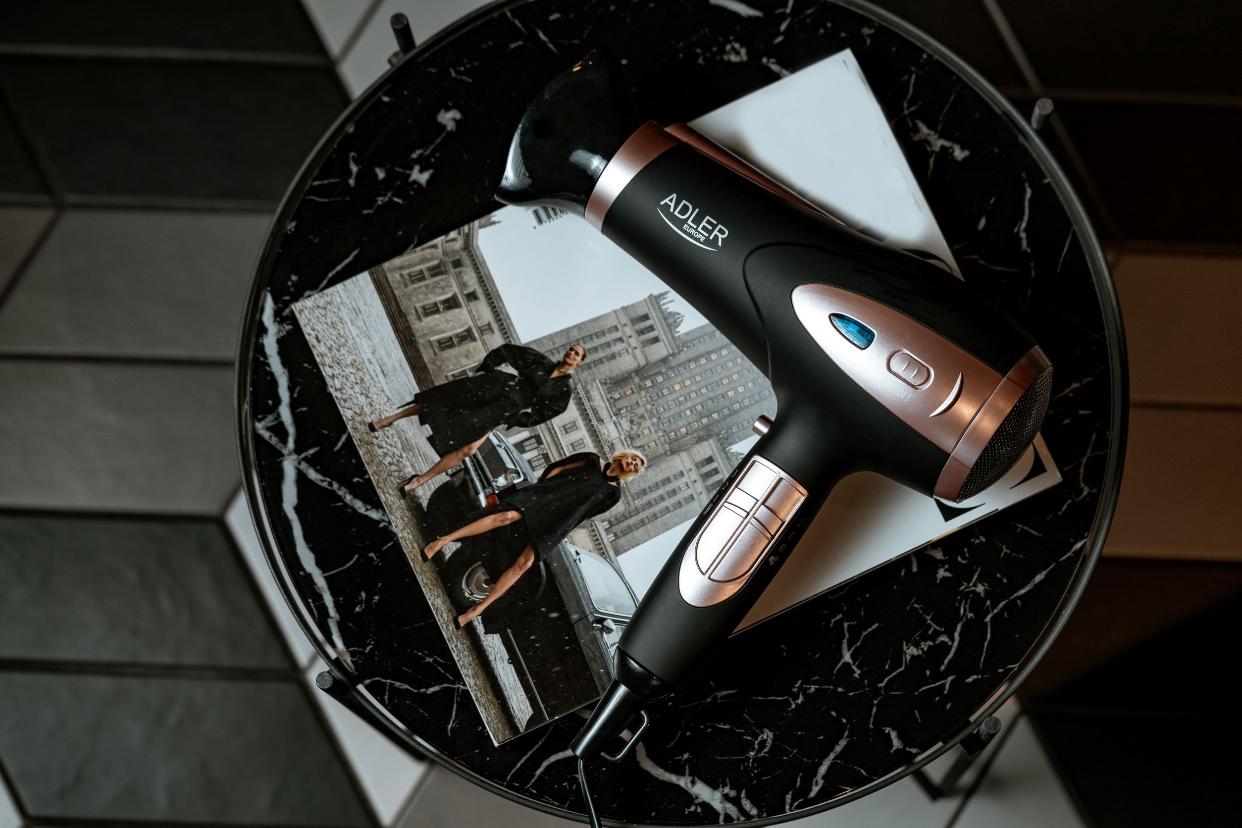 Czarna i różowo-złota suszarka do włosów na marmurowym stole, z magazynem, widok z góry.