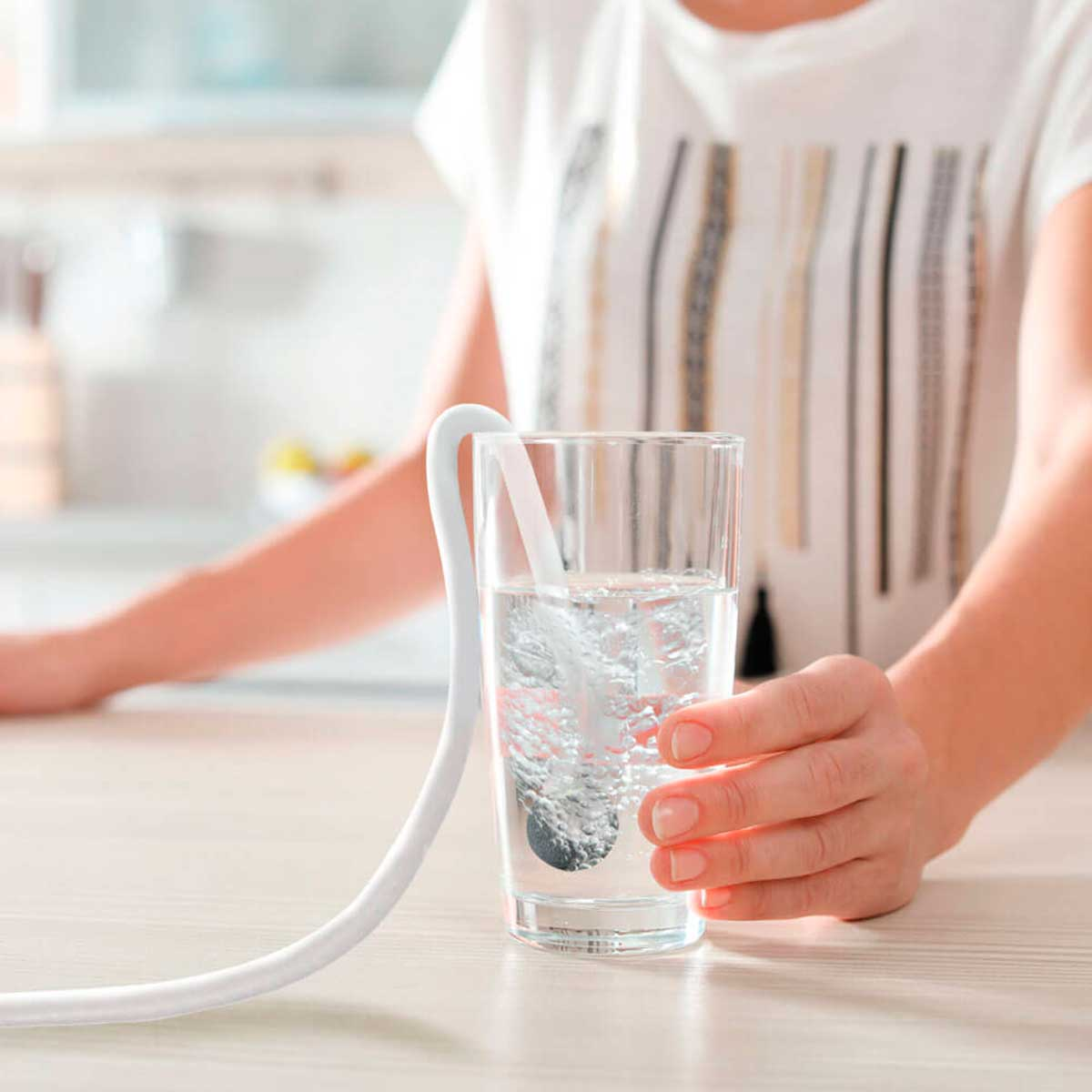Mano sosteniendo un vaso con agua y un tubo blanco.