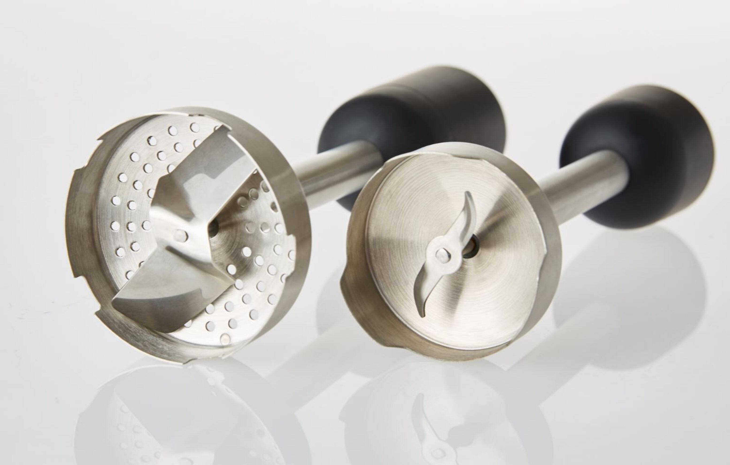 Due accessori per frullatore in acciaio inossidabile con diversi design di lame, posizionati su una superficie bianca.