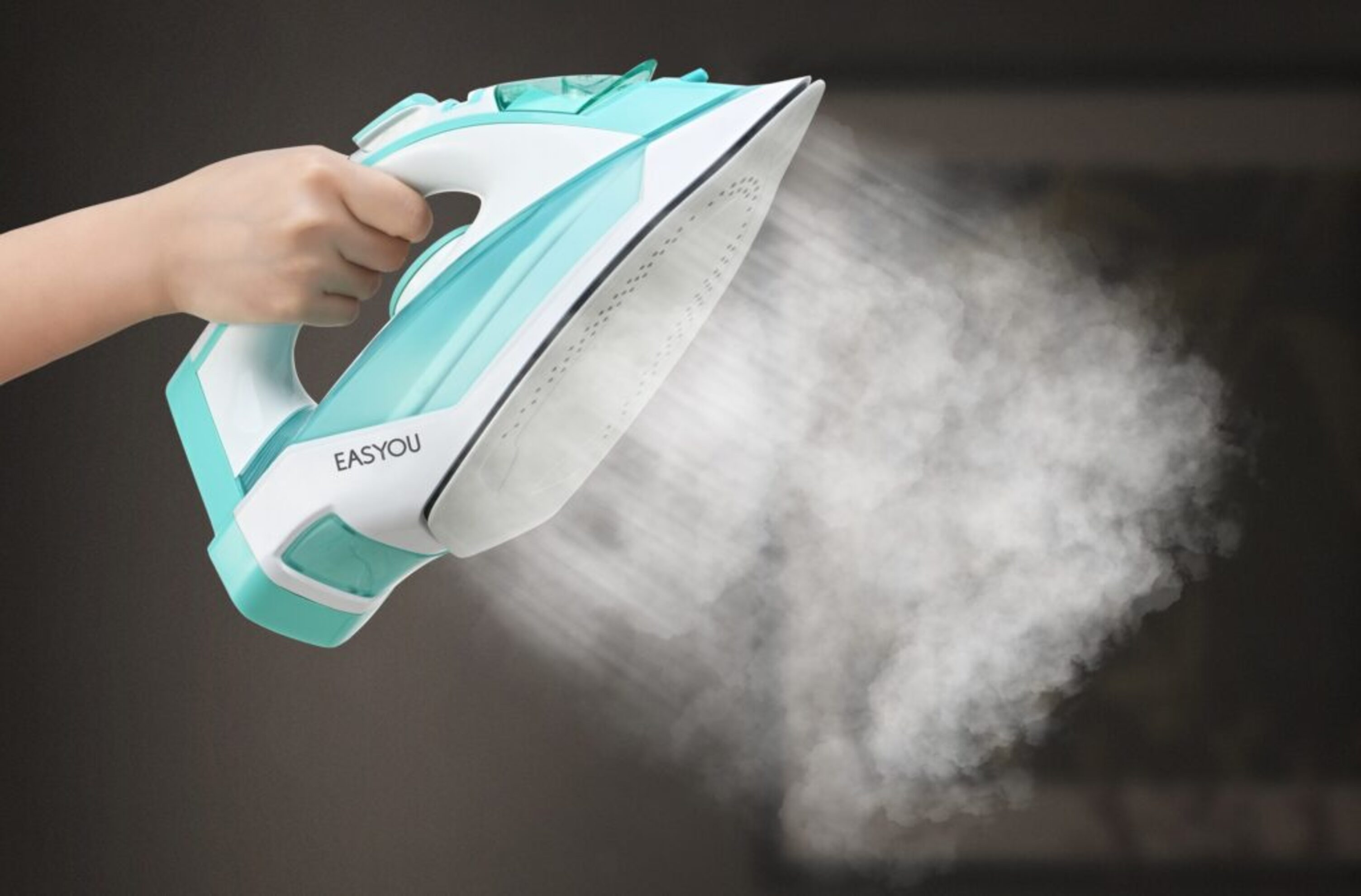 Una plancha rociando vapor, sostenida por una mano, sobre un fondo borroso.