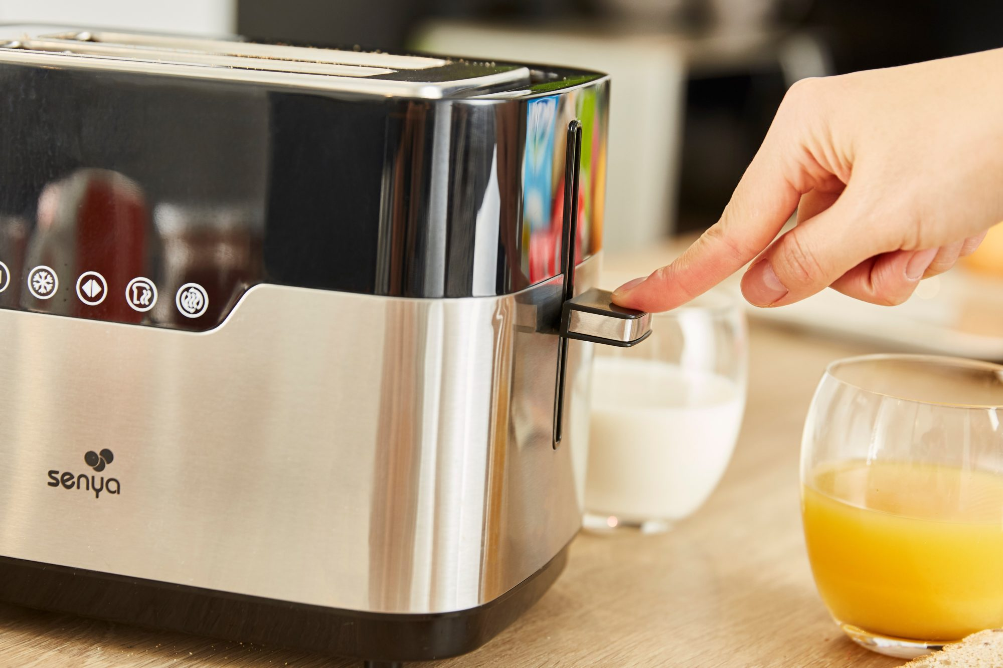 Ein silberner und schwarzer Toaster mit einer Hand, die den Hebel drückt. Gläser daneben.