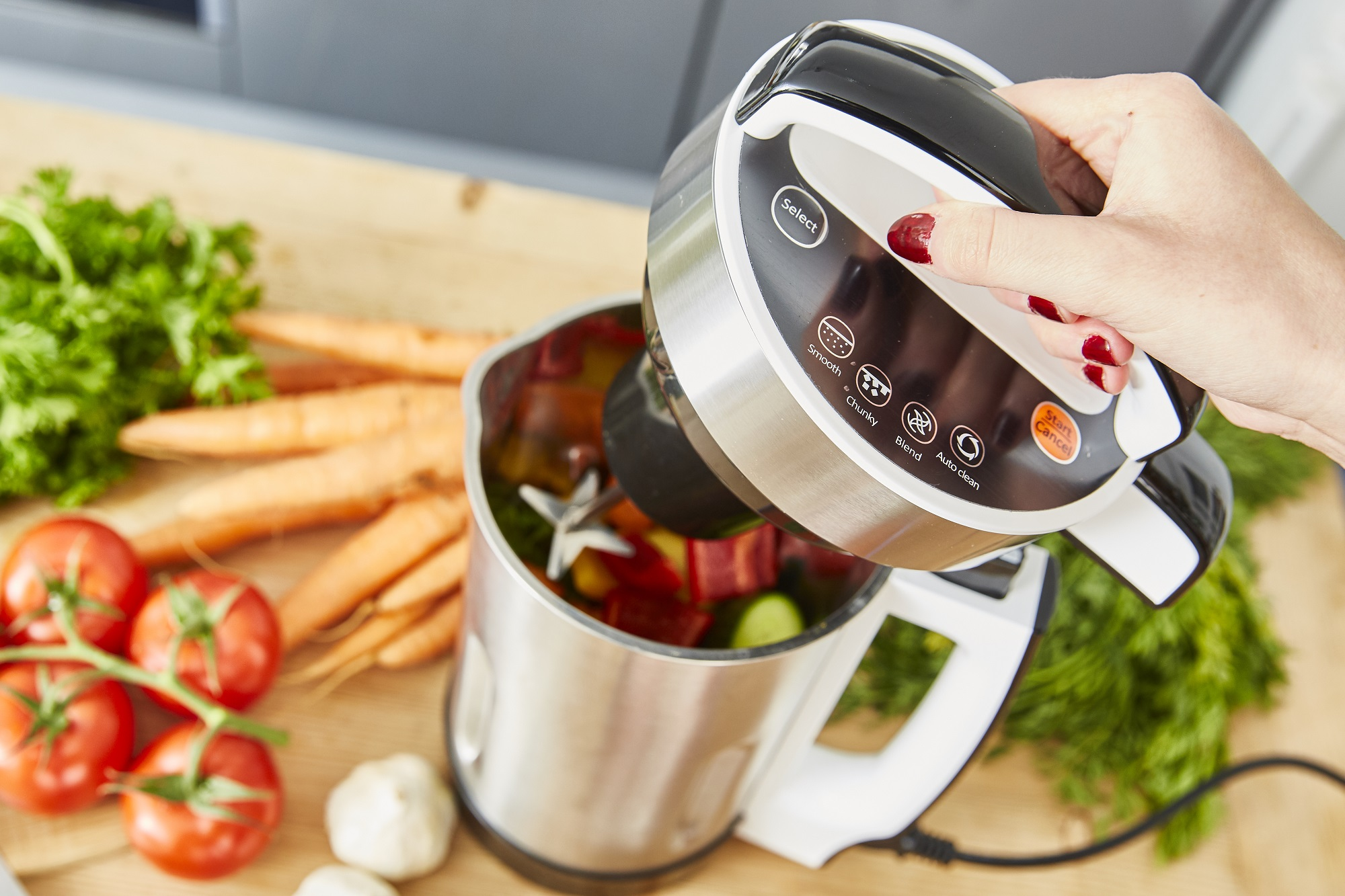 Frau fügt Zutaten in Mixer mit Karotten und Gemüse hinzu.