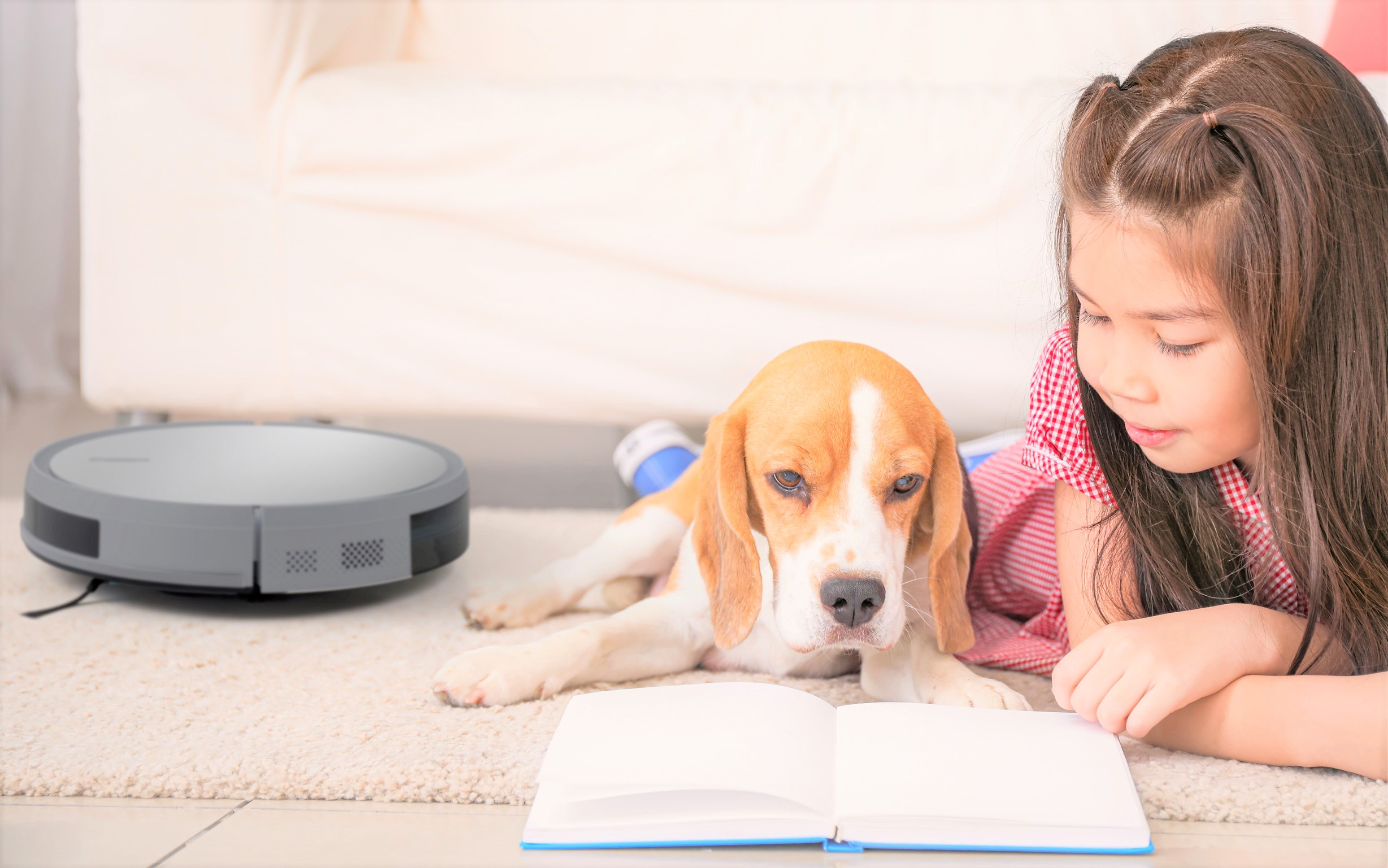 Ein Mädchen und ein Hund lesen zusammen ein Buch, neben einem Roboter-Staubsauger auf einem Teppich.