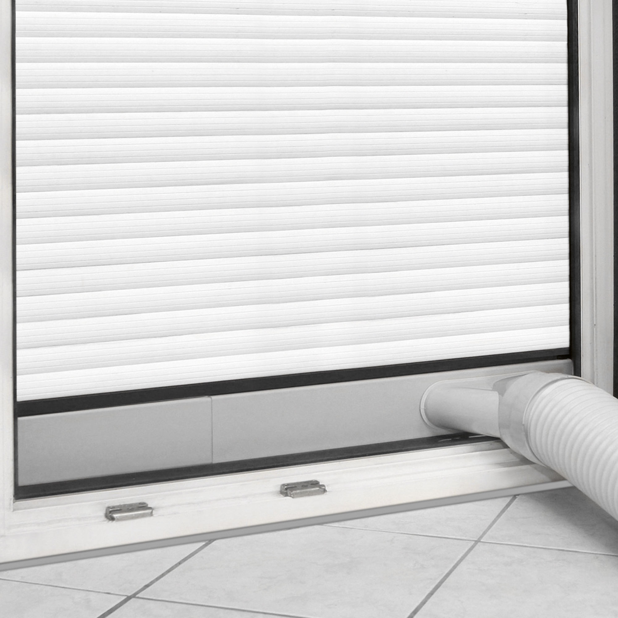Ventana blanca con persiana enrollable corrugada blanca. Un tubo flexible blanco se extiende desde ella.