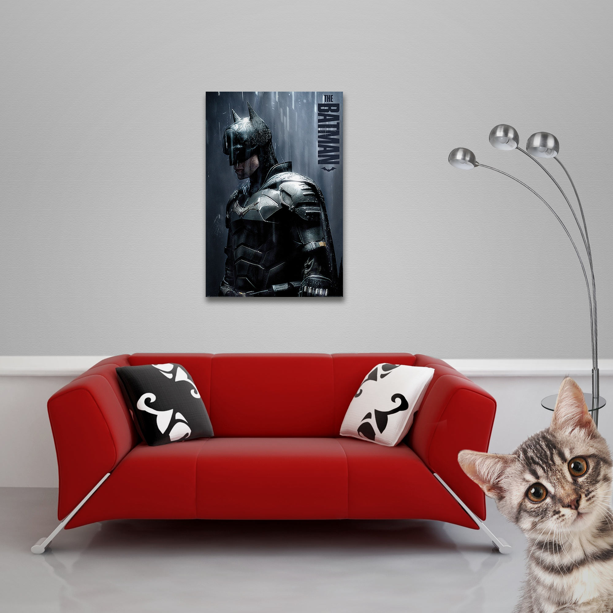 The Batman Poster an einer Wand über einem roten Sofa. Eine Katze im Vordergrund rechts.