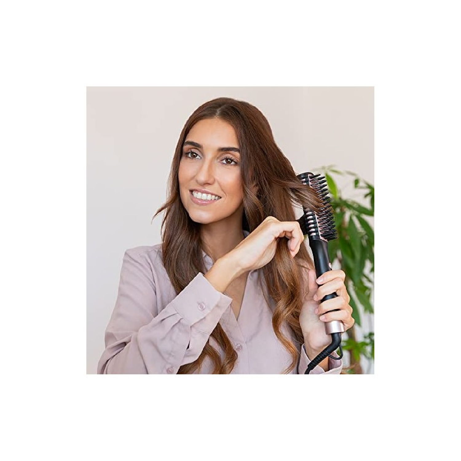 Vrouw borstelt haar haar met een krulborstel. Ze glimlacht, met een groene plant op de achtergrond.