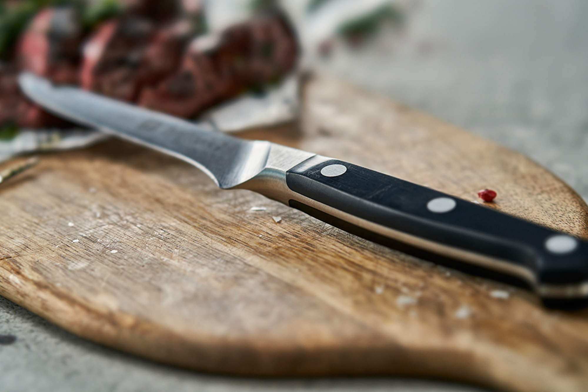 Nóż na drewnianej desce do krojenia. Nóż ma czarną rękojeść i leży obok jedzenia.