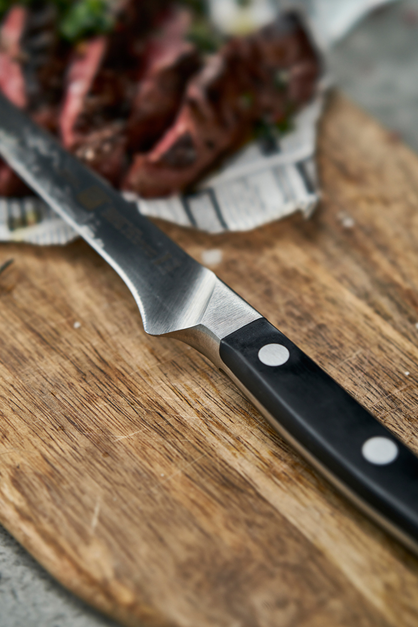 Zbliżenie noża na drewnianej desce do krojenia z jedzeniem. Nóż ma czarny uchwyt i srebrne ostrze.
