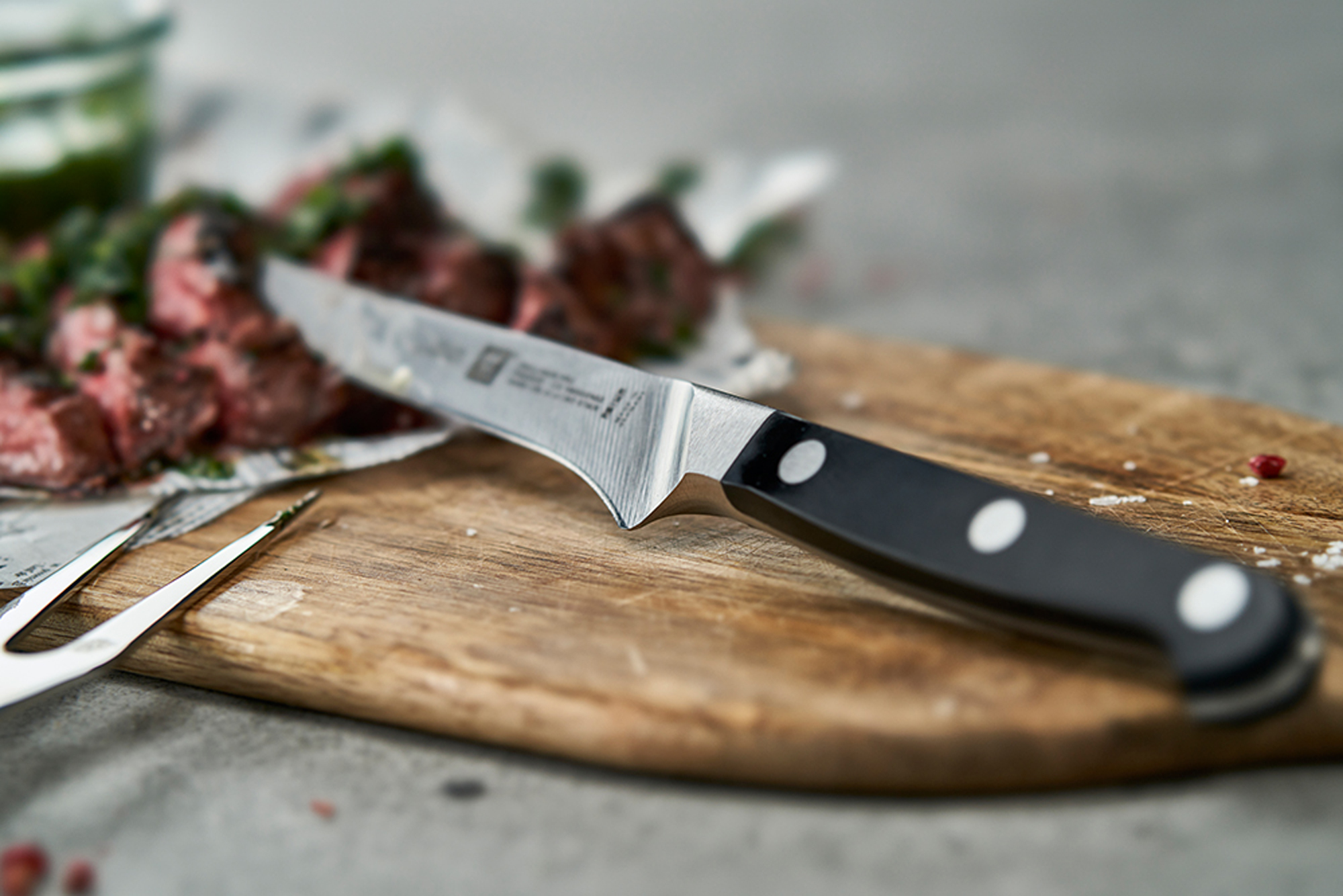 Nóż na drewnianej desce do krojenia, mięso na desce. Nóż ma czarny uchwyt i srebrne ostrze.