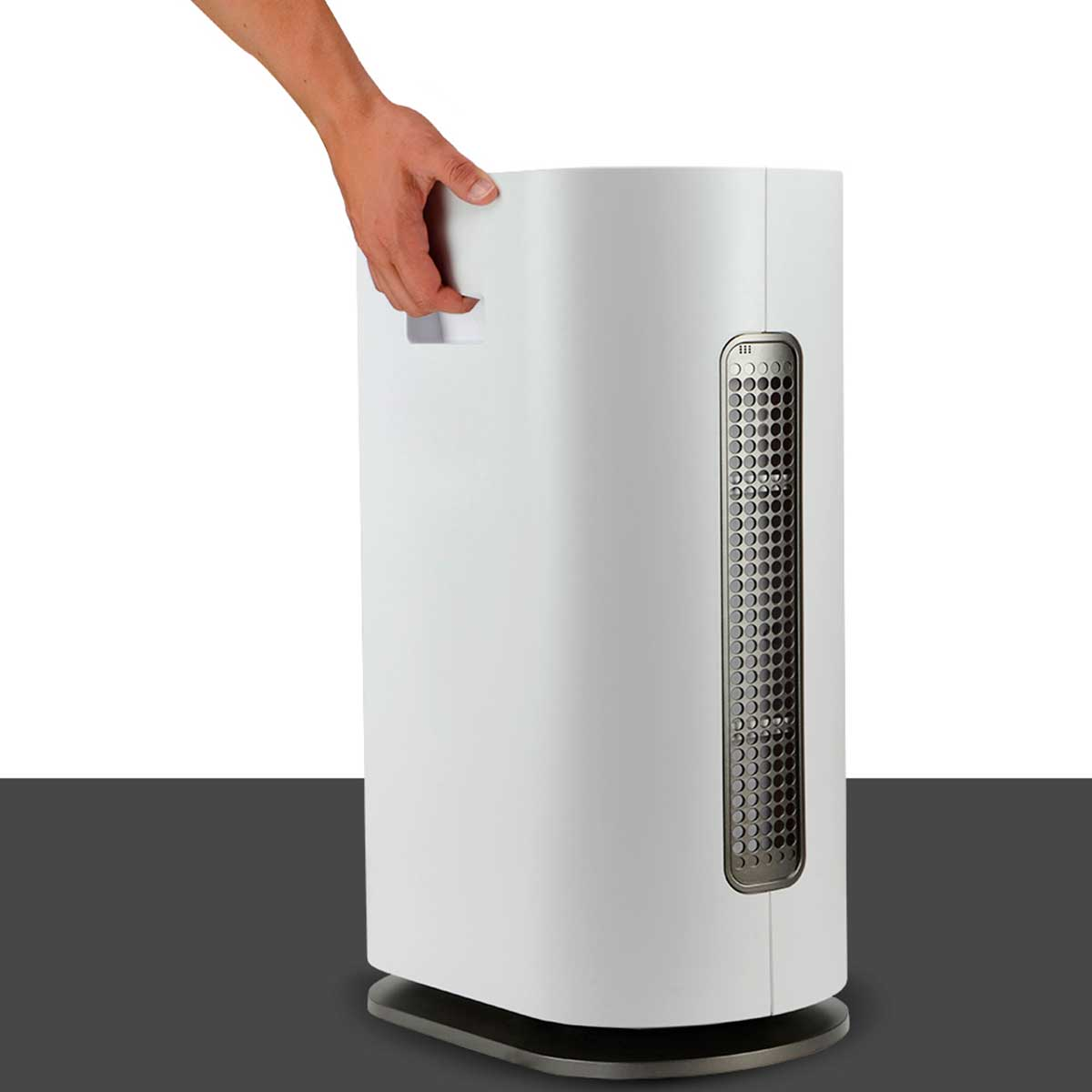 Purificador de aire blanco con una mano sujetando la parte superior. Está sobre superficie oscura.