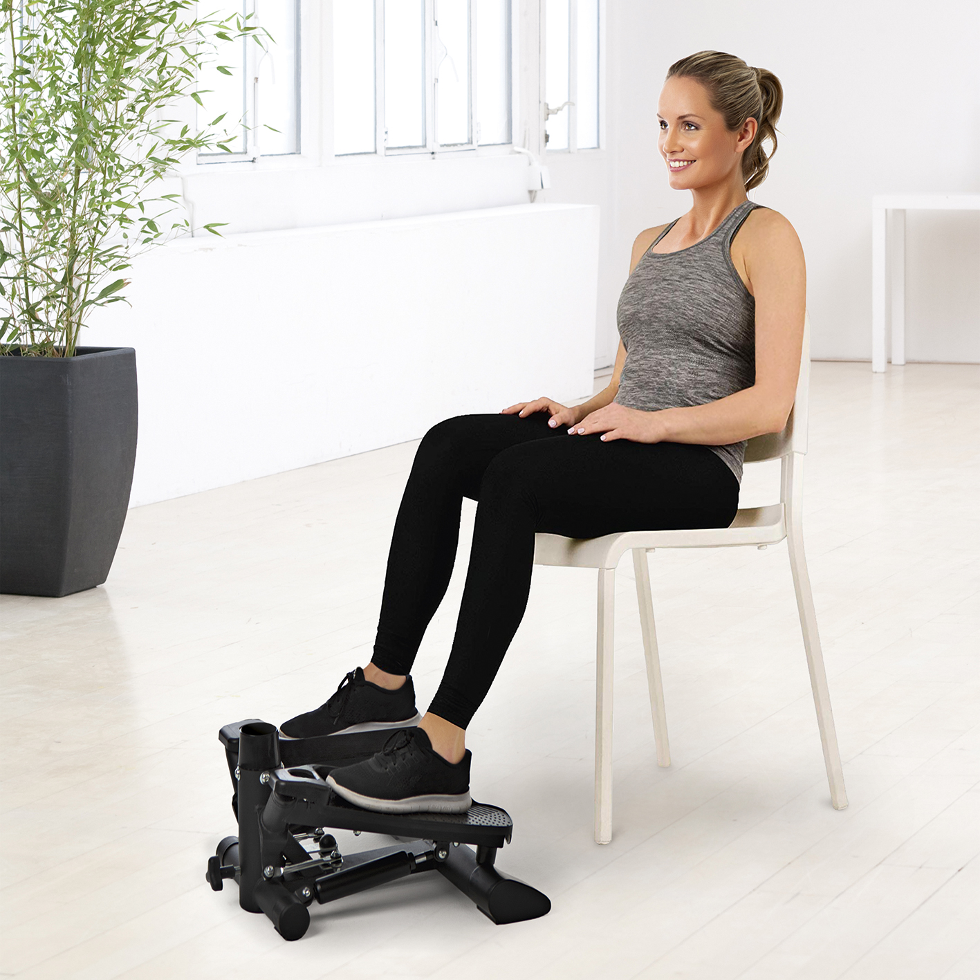 Frau auf einem Stepper, sitzend auf einem Stuhl. Weißer Hintergrund mit Pflanze.