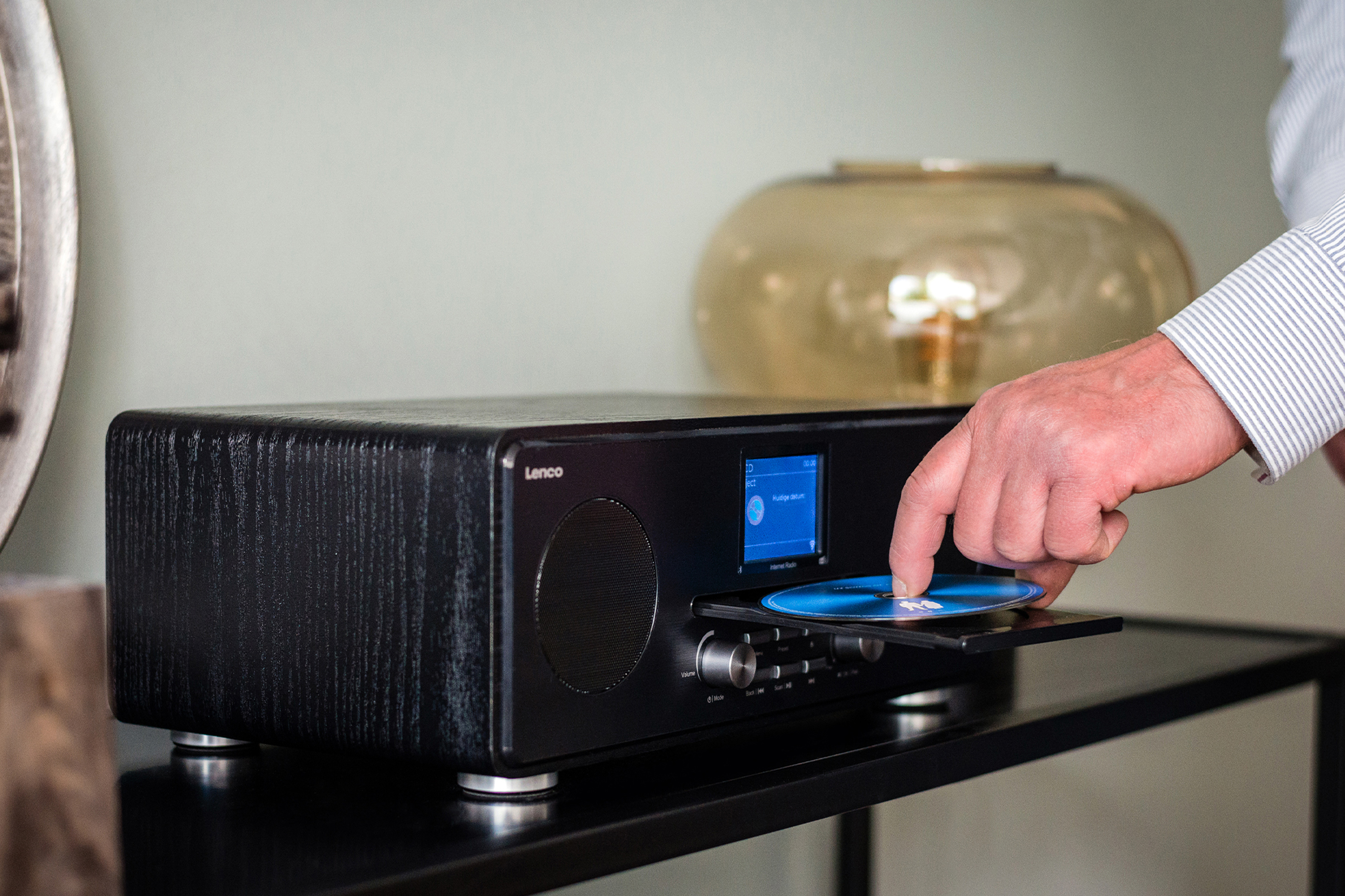 Mężczyzna wkłada płytę CD do czarnego drewnianego odtwarzacza audio. Widoczny jest niebieski ekran.