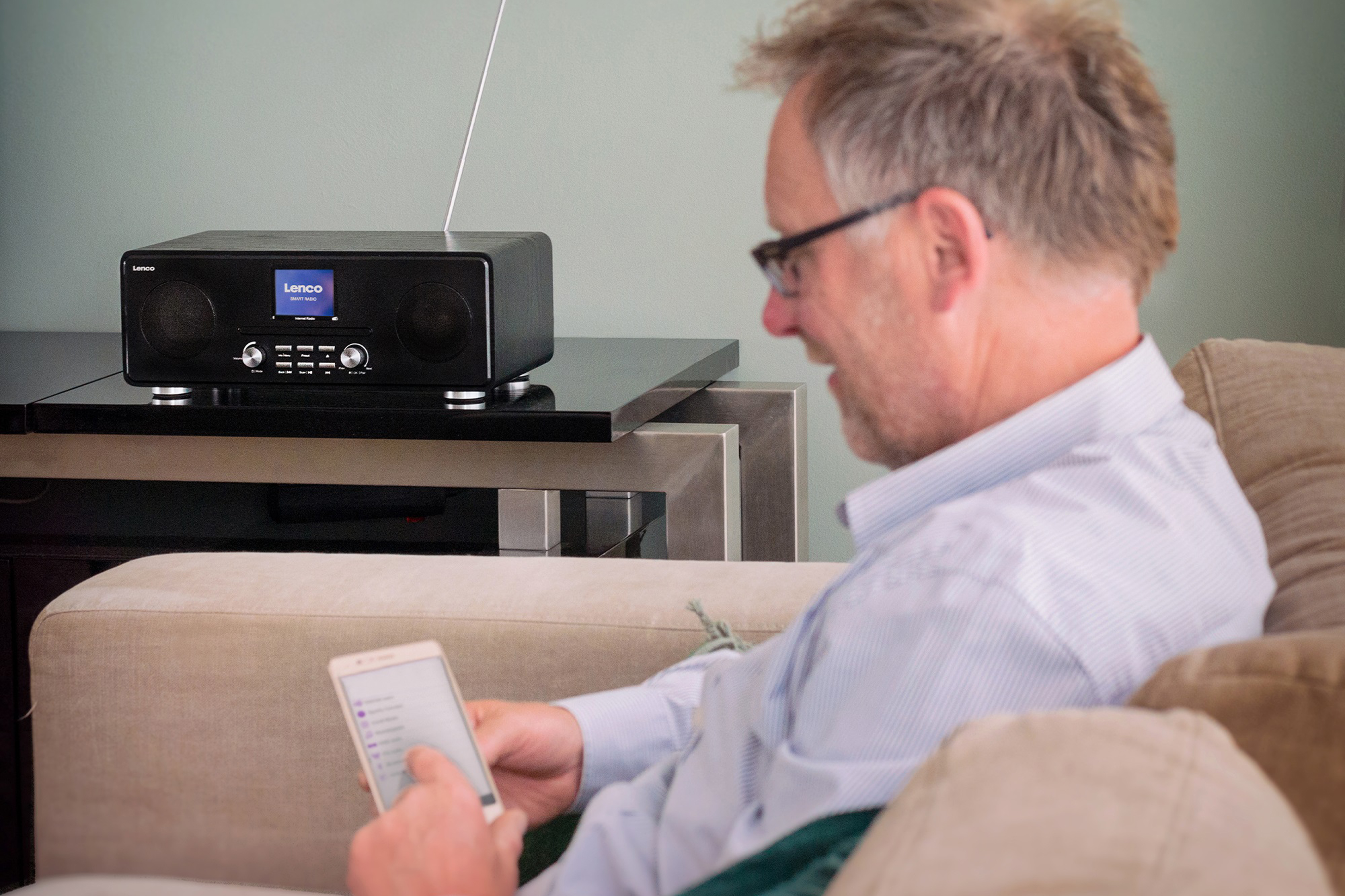 Mężczyzna korzystający z tabletu siedząc na kanapie, radio na stole w tle. Pokój ma zielone ściany.