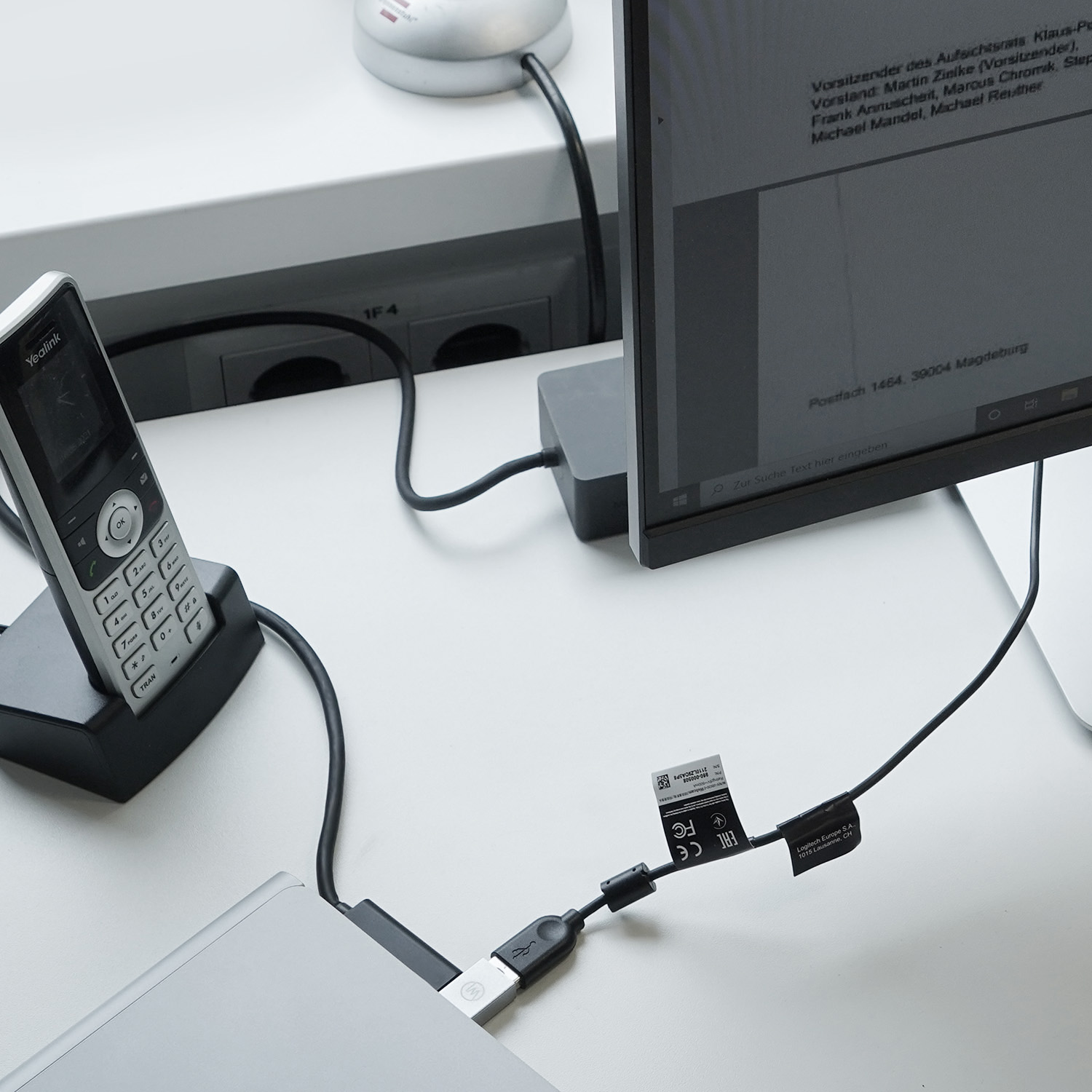 Ein Schreibtisch-Setup mit einem Computermonitor, Telefon und einem Laptop, der mit Kabeln verbunden ist.