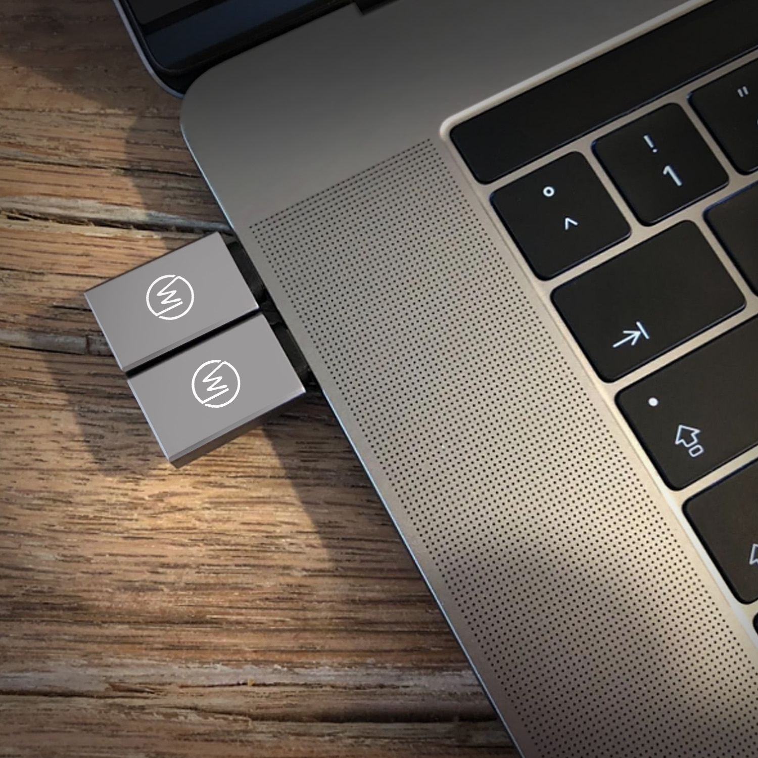 Zwei silberne USB-Laufwerke in der Nähe eines Laptops auf einem Holztisch, mit dem 'W'-Logo auf jedem.