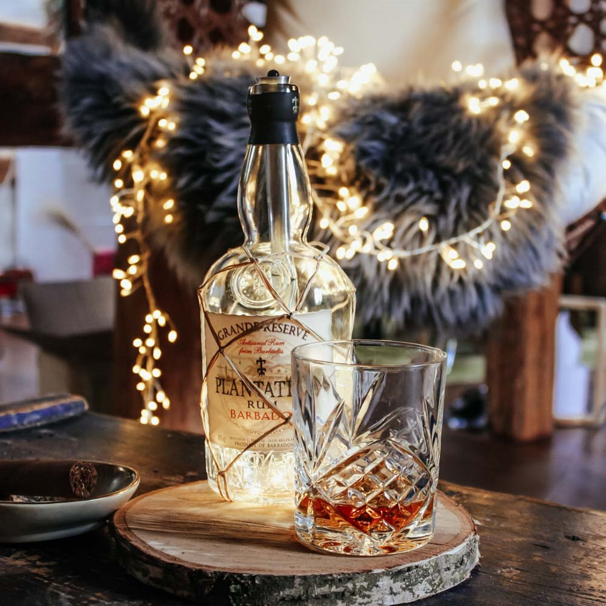 Rumflasche mit einem Glas. Ein Holztablett und Lichterketten im Hintergrund.