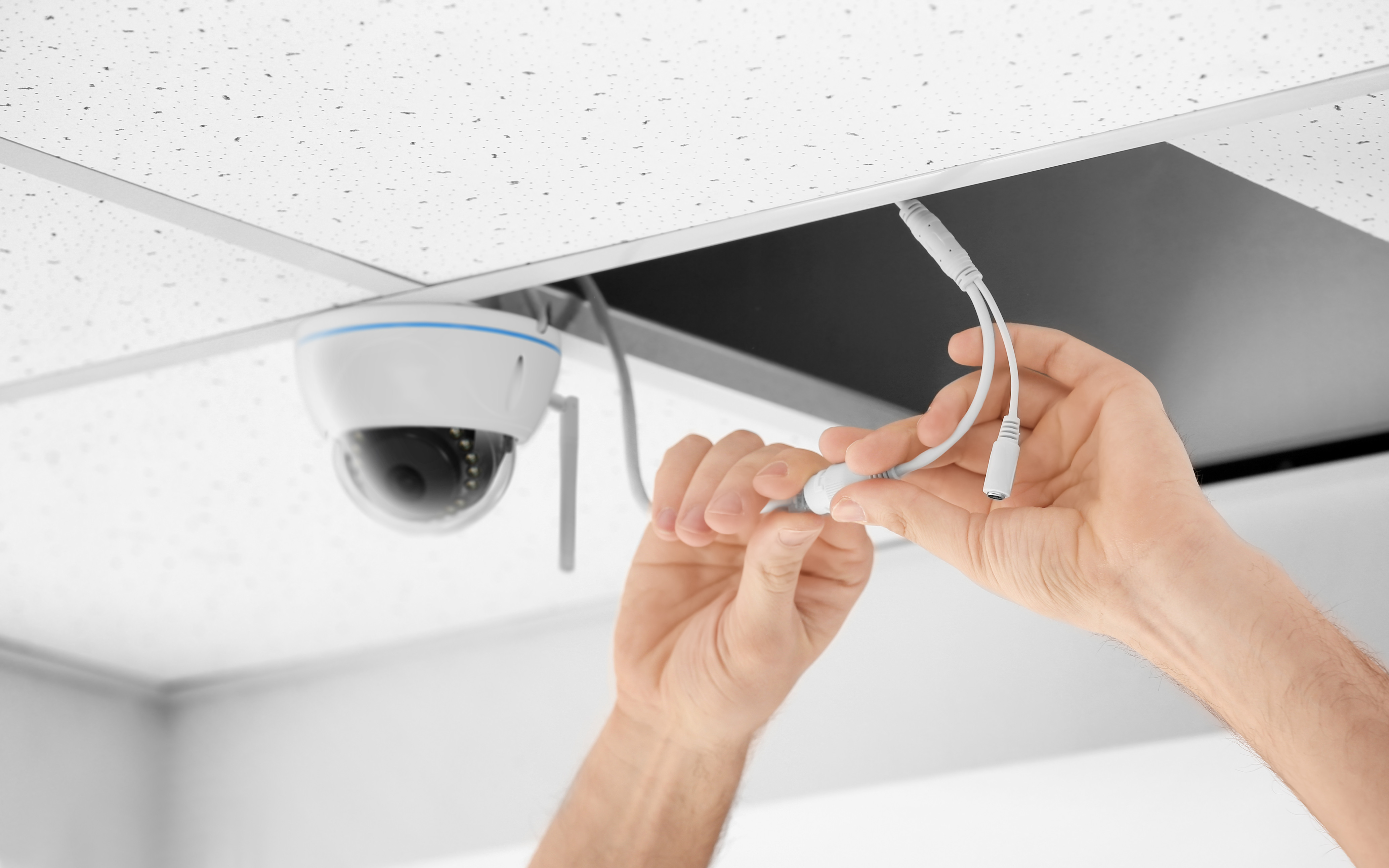 Eine Person verbindet die Kabel einer Überwachungskamera mit einer Deckenplatte.