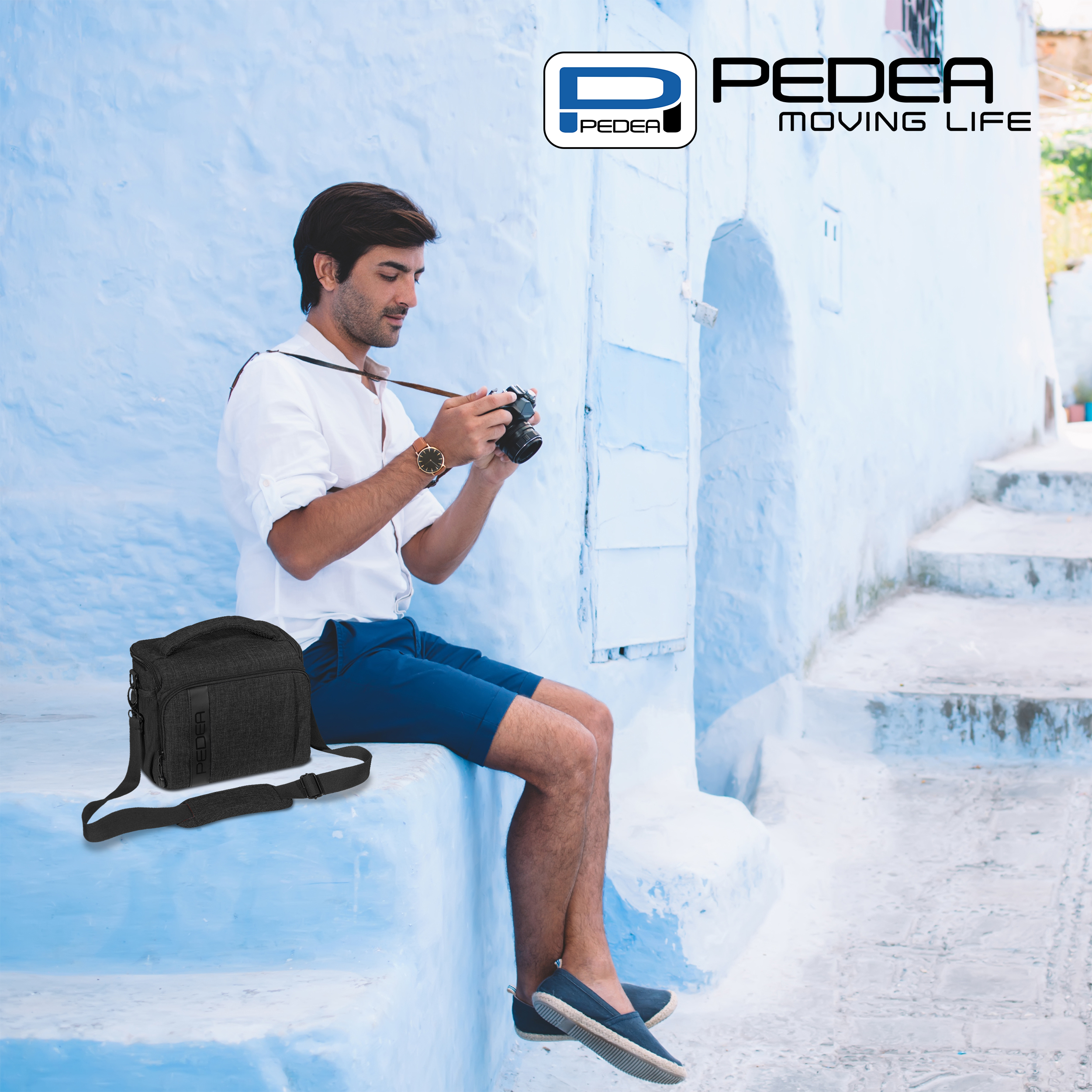 Ein Mann sitzt auf blauen Treppen in einem weißen Hemd und macht ein Foto mit einer Kamera. Eine schwarze Tasche ist in der Nähe.