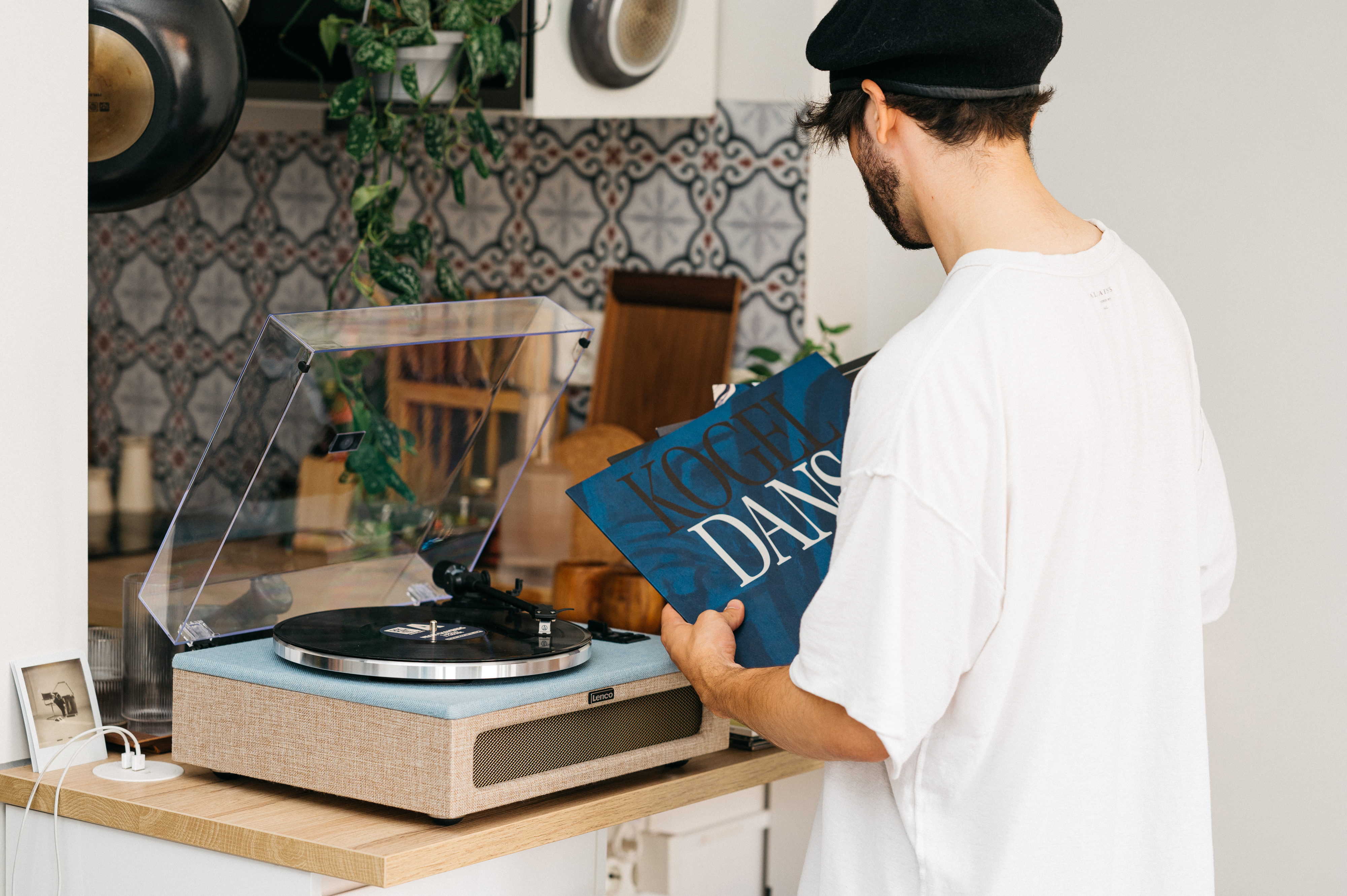 Man in een wit shirt, houdt vinylplaten vast bij een platenspeler, met een lichtblauwe basis.