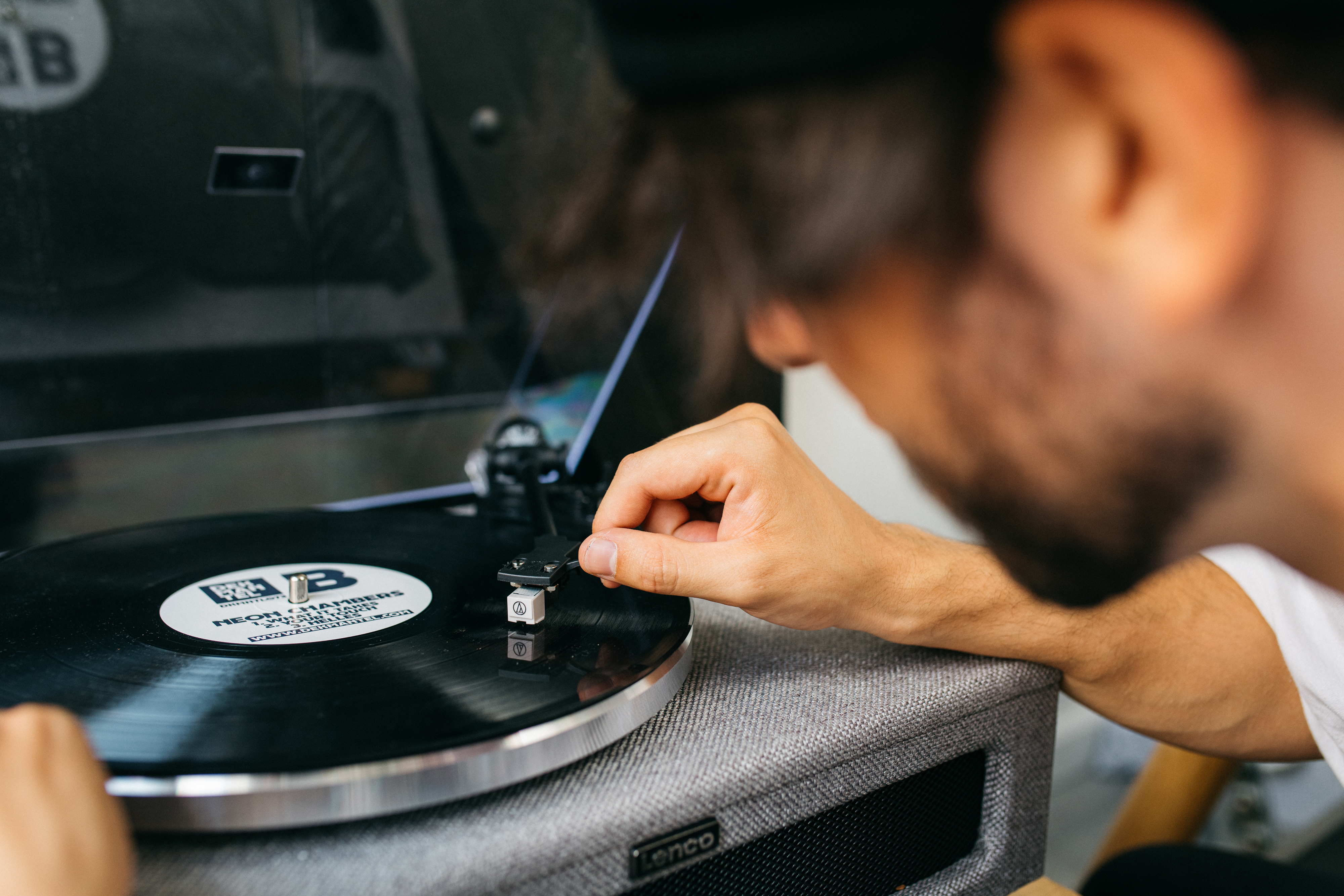 Un hombre ajustando la aguja de un tocadiscos, con un disco de vinilo reproduciéndose.
